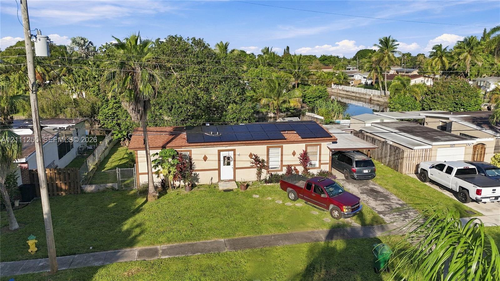 Single-story residence featuring rooftop solar panels, a covered carport, and a manicured front lawn