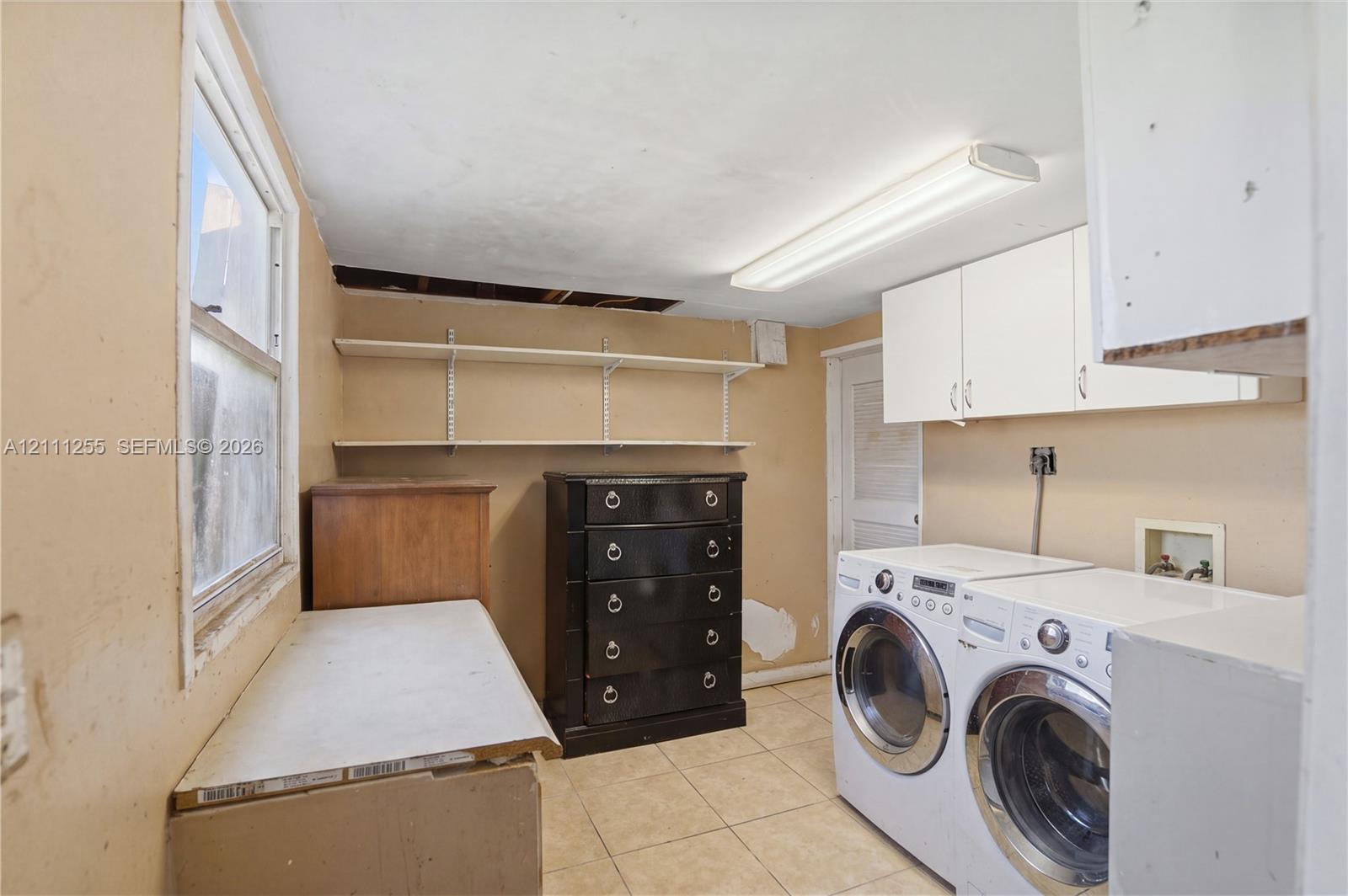 Laundry space featuring wall-mounted upper cabinetry, open shelving, and tile flooring