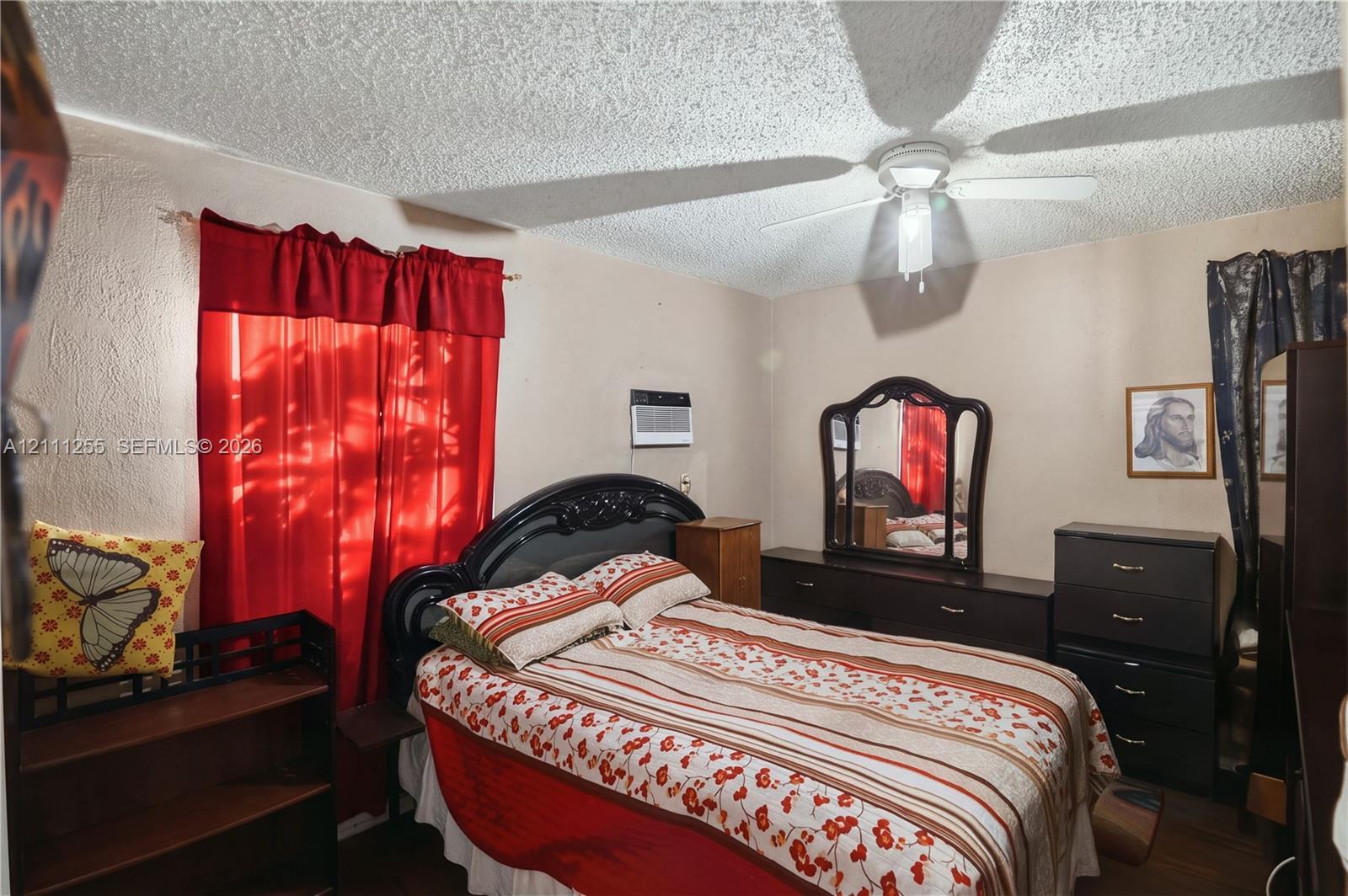Textured ceiling with a central multi-blade ceiling fan and wall-mounted air conditioning unit