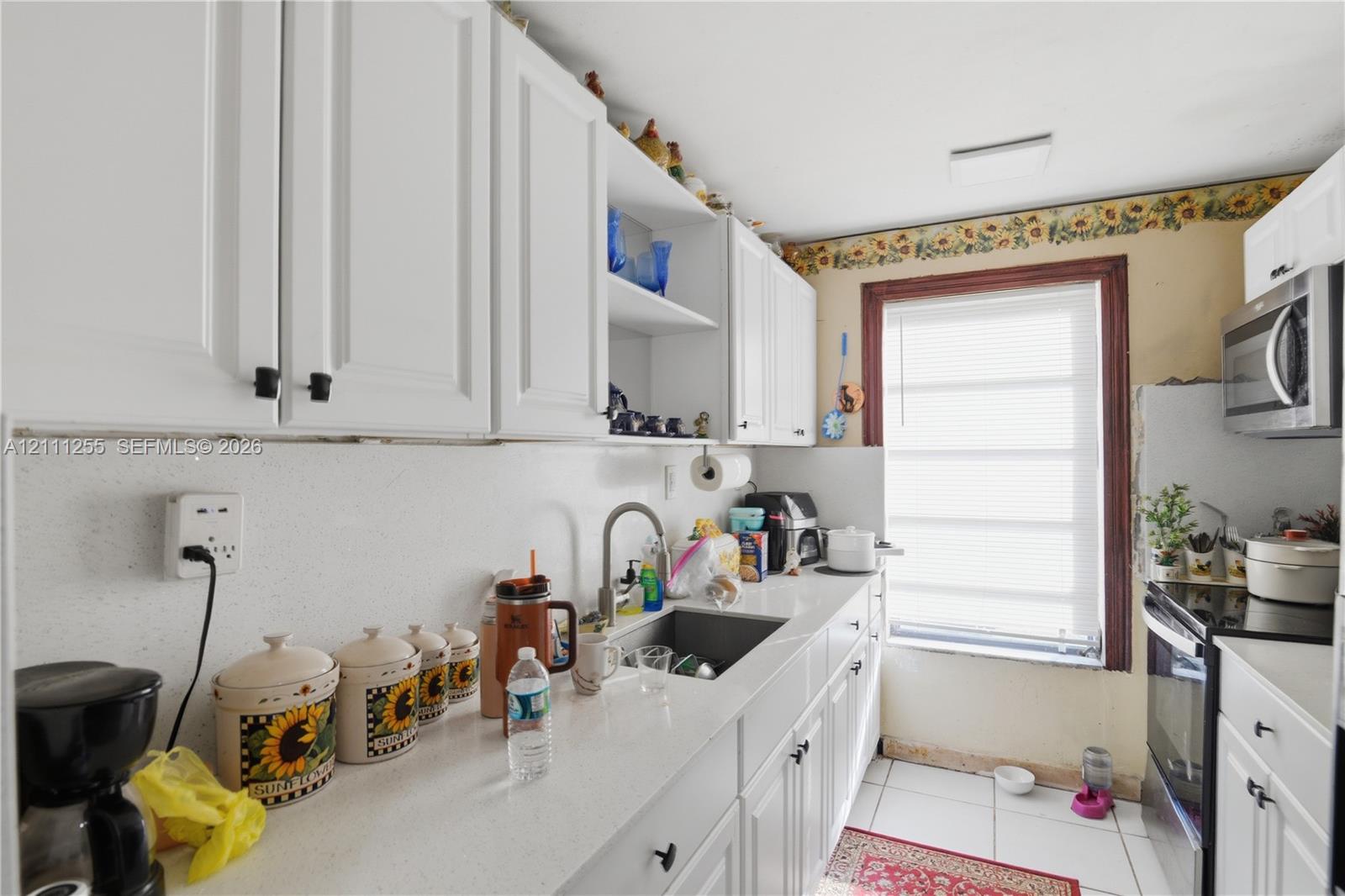 Kitchen featuring white cabinetry, stone-finish countertops, stainless steel sink with a high-arc faucet, and built-in stainless steel microwave