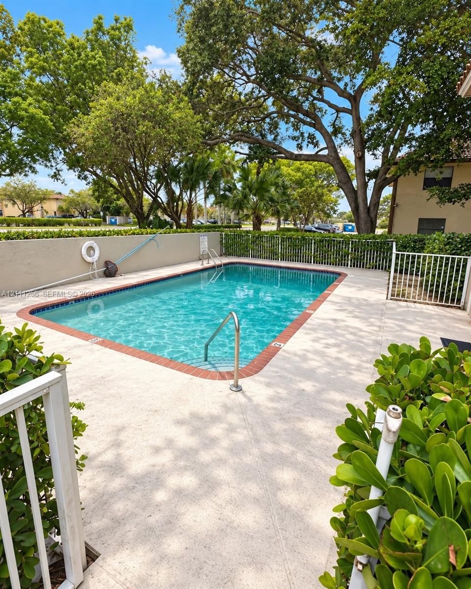 Rectangular swimming pool featuring a brick-tiled border, metal handrail, concrete patio surround, and white perimeter fencing Rectangular swimming pool featuring a brick-tiled border, metal handrail, concrete patio surround, and white perimeter fencing