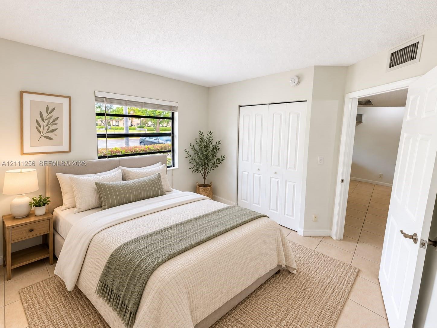 Neutral-toned interior space featuring light-colored tile flooring, a horizontal slider window, and built-in closet cabinetry with dual folding doors Neutral-toned interior space featuring light-colored tile flooring, a horizontal slider window, and built-in closet cabinetry with dual folding doors