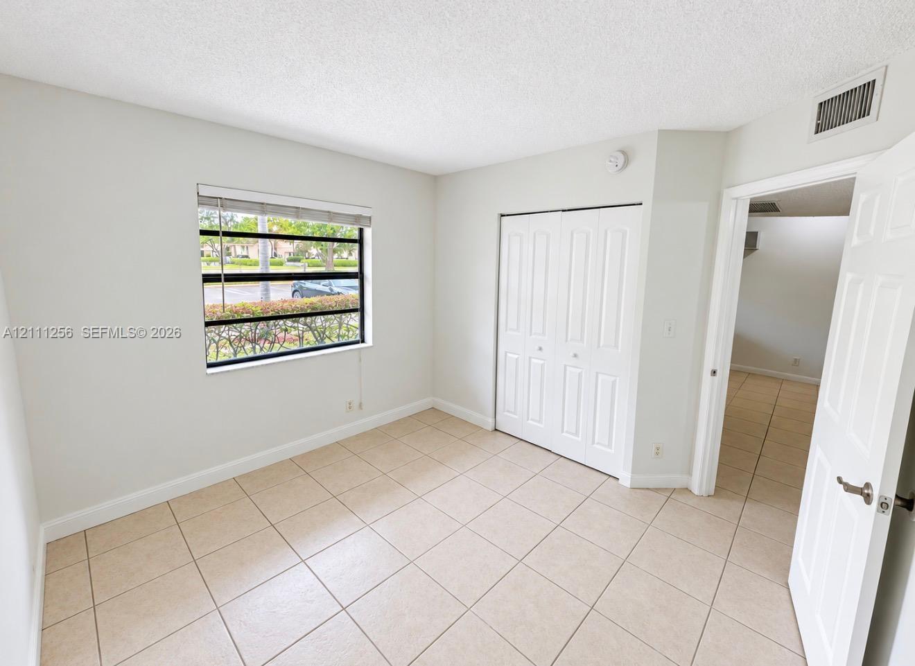 Neutral-toned room featuring tile flooring, a large single-pane window, and a built-in closet with double bifold doors Neutral-toned room featuring tile flooring, a large single-pane window, and a built-in closet with double bifold doors