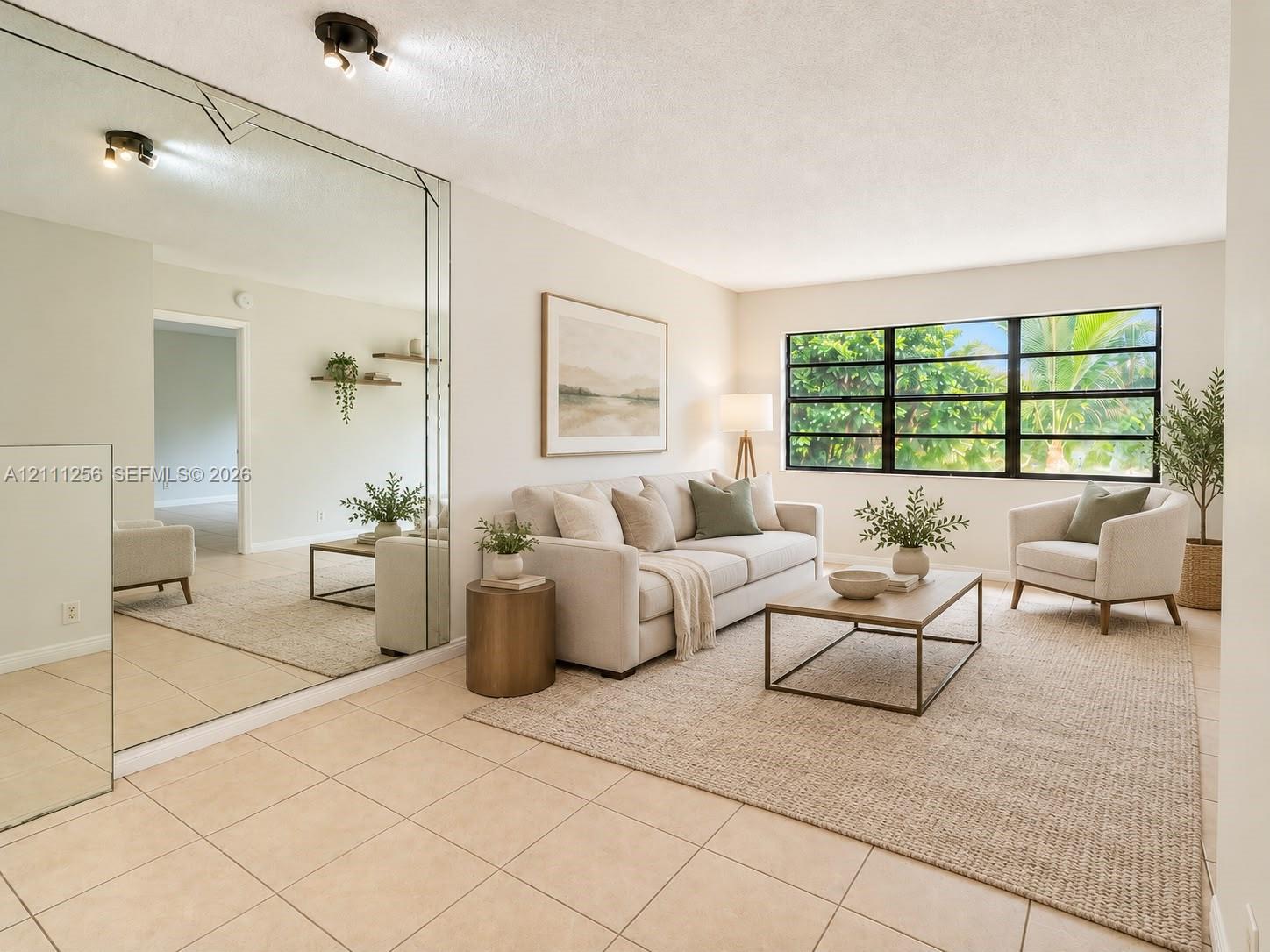 Living area featuring neutral tile flooring, large multi-pane windows with black frames, and a floor-to-ceiling mirrored wall Living area featuring neutral tile flooring, large multi-pane windows with black frames, and a floor-to-ceiling mirrored wall