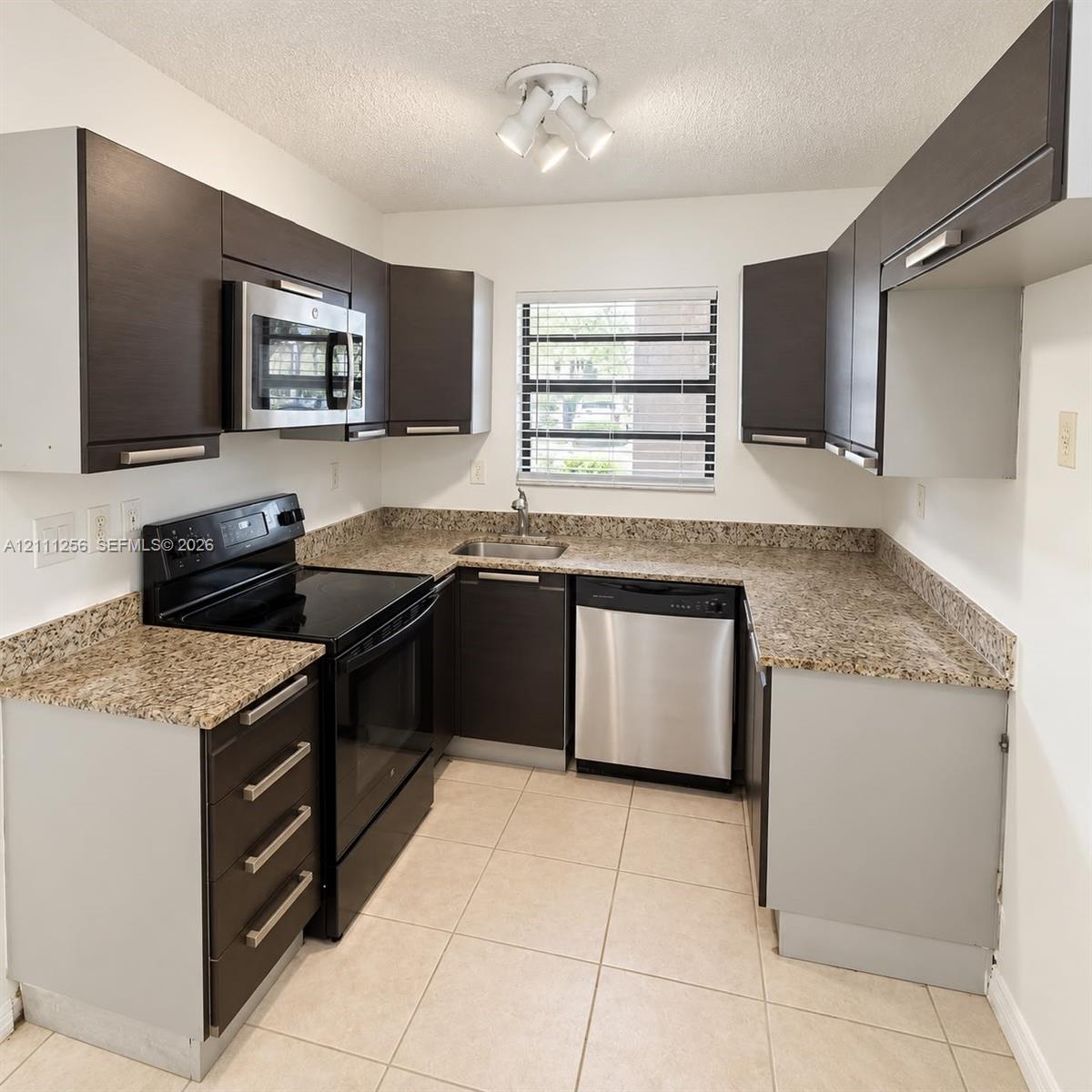 Kitchen featuring dark cabinetry, stone-finish countertops, stainless steel appliances, tile flooring, and multi-light ceiling fixture Kitchen featuring dark cabinetry, stone-finish countertops, stainless steel appliances, tile flooring, and multi-light ceiling fixture
