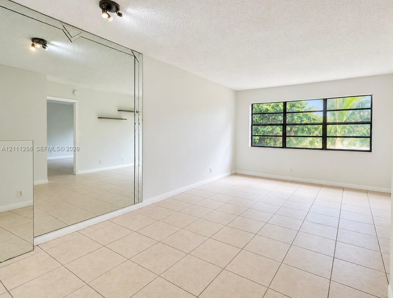 Neutral-toned tile flooring, floor-to-ceiling wall mirror, large multi-pane window, built-in wall shelving, and two ceiling-mounted light fixtures Neutral-toned tile flooring, floor-to-ceiling wall mirror, large multi-pane window, built-in wall shelving, and two ceiling-mounted light fixtures