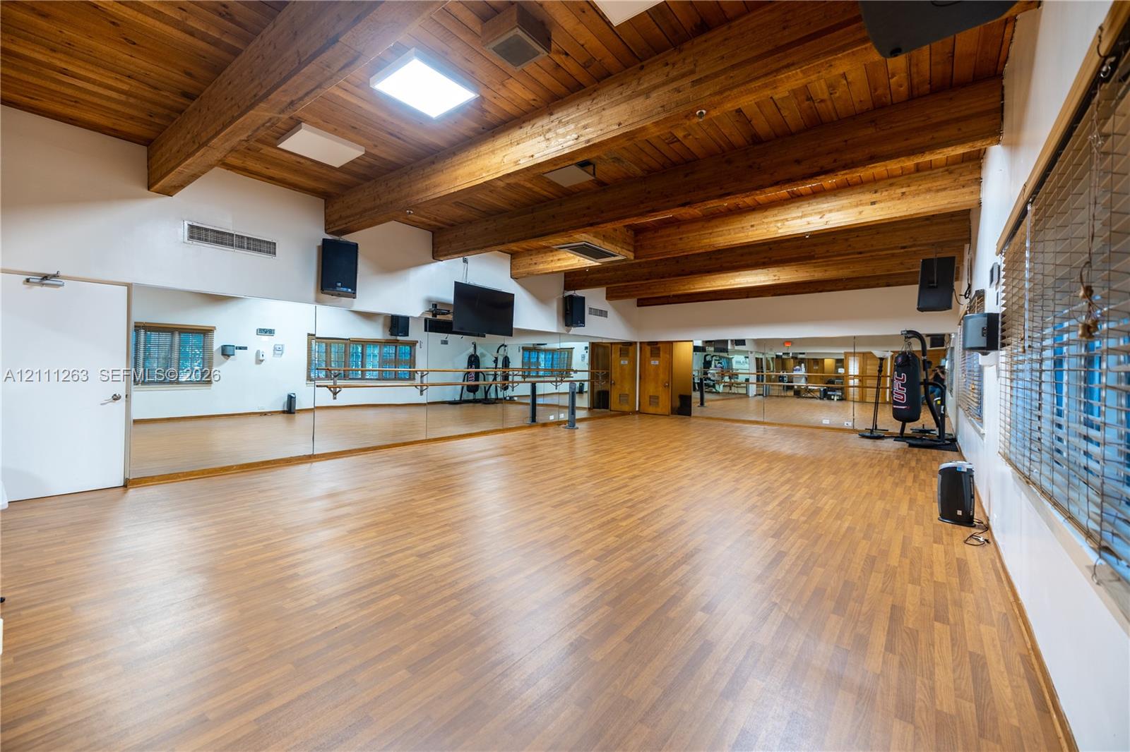 Expansive room featuring vaulted wood-plank ceilings with exposed timber beams, wood-finish flooring, full-length wall mirrors, and a wall-mounted ballet barre