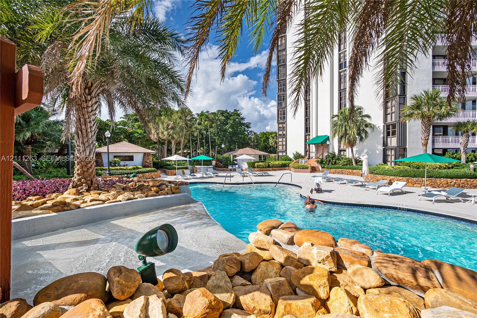 Swimming pool featuring a sun shelf entry, natural stone hardscaping, tropical landscaping, and structural shade coverings