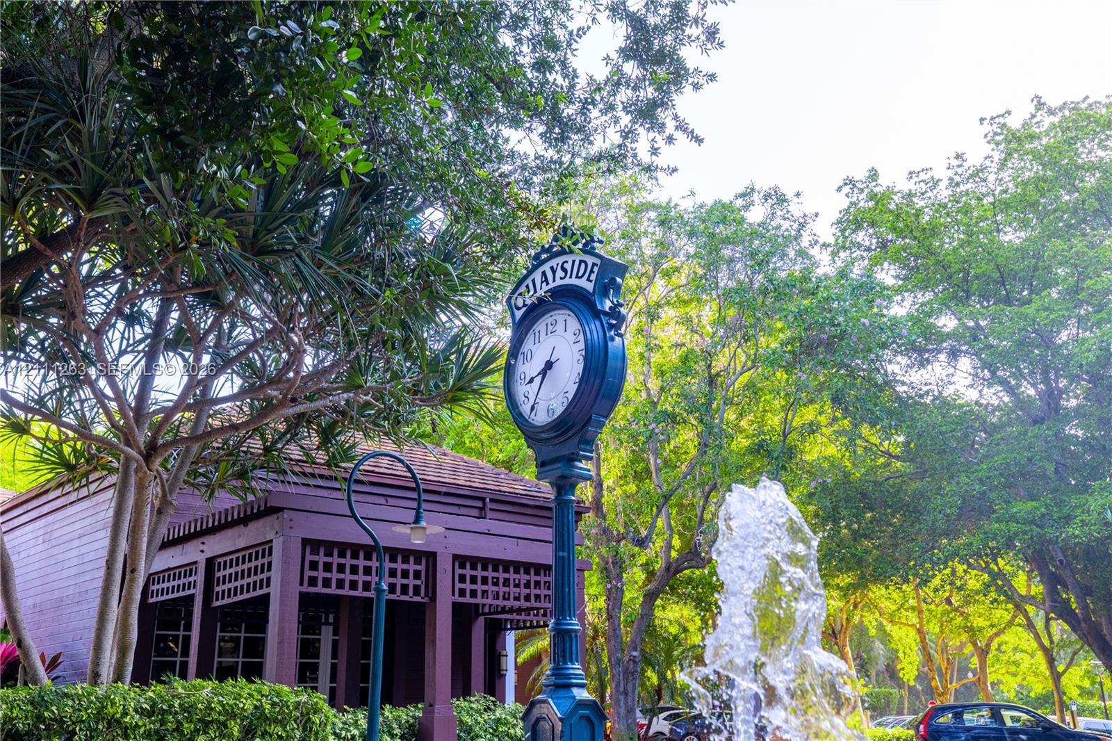 Landscaped grounds featuring a water fountain, decorative clock post, mature trees, and a wooden structure with lattice detailing