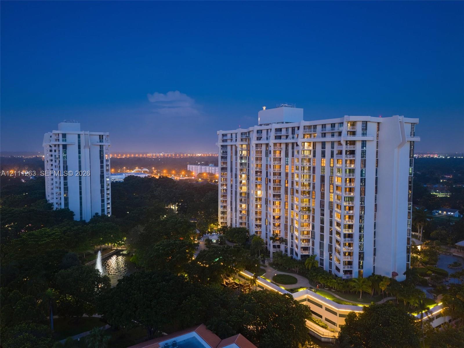 High-rise residential architecture featuring private balconies, integrated building lighting, and surrounding landscaped grounds with a water feature