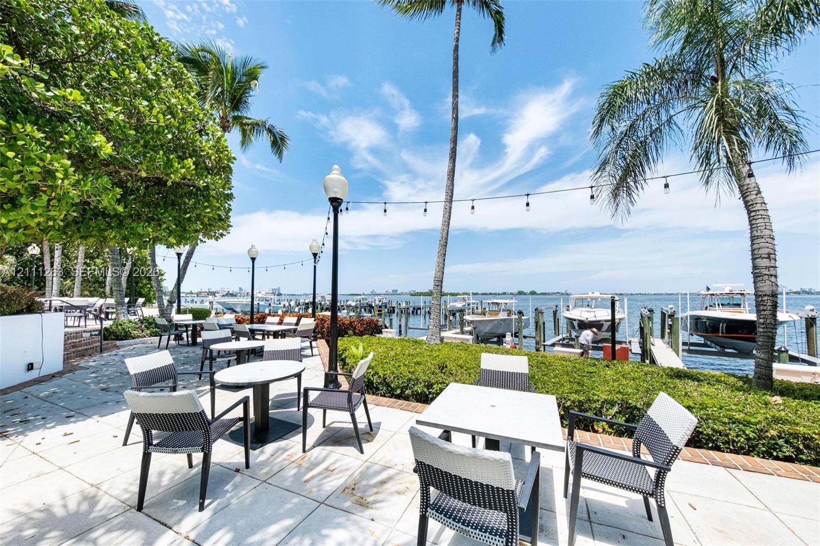 Waterfront patio featuring stone paver flooring, integrated landscape lighting, established palm trees, and a private boat dock