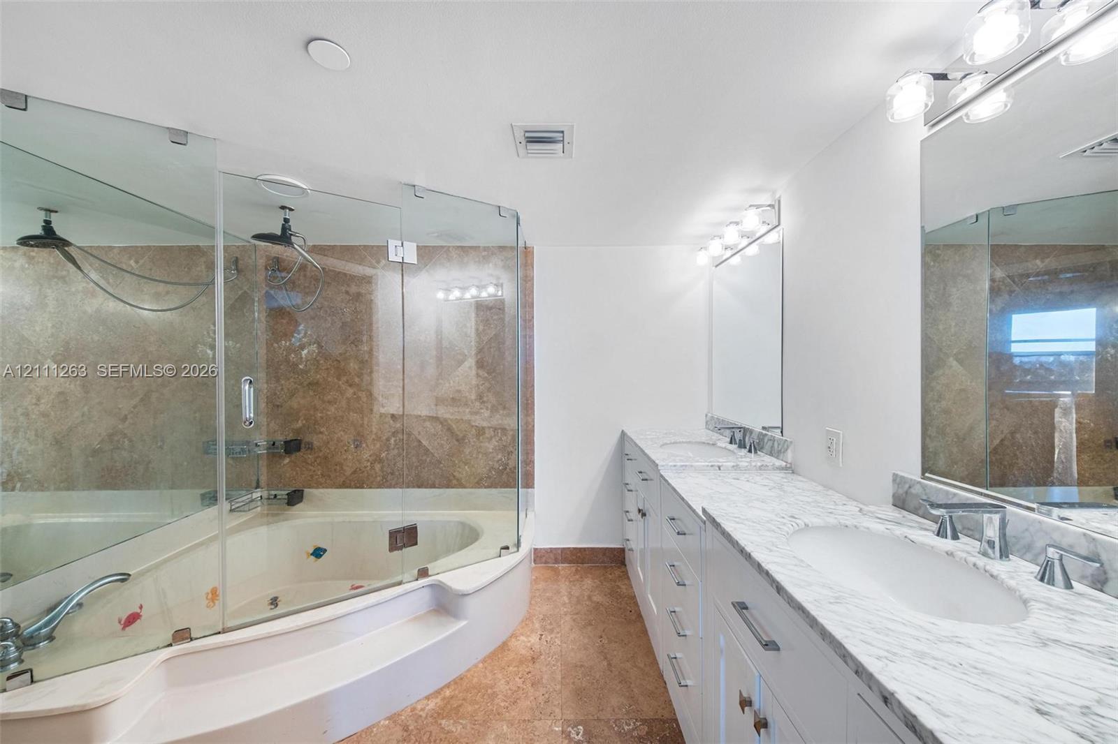 Bathroom featuring a dual-sink vanity with stone countertops, white cabinetry, a glass-enclosed shower, and a built-in jetted tub with stone tile surround