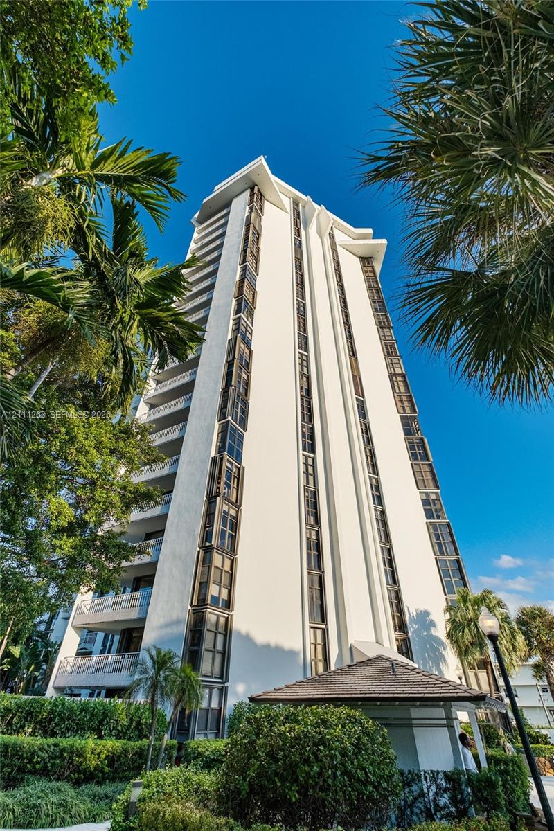 High-rise residential exterior featuring a white stucco facade, vertical window banks, private balcony tiers, and mature palms