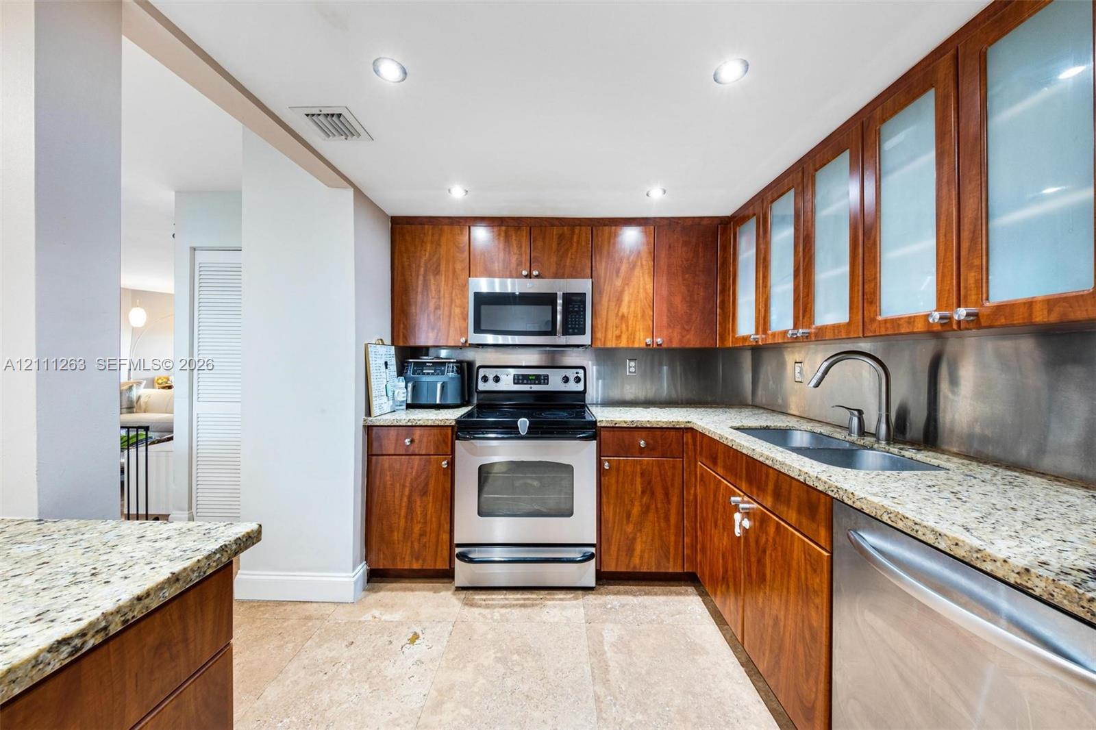 Kitchen featuring wood cabinetry with glass-panel uppers, stone-finish countertops, stainless steel appliances, a metallic backsplash, and recessed lighting