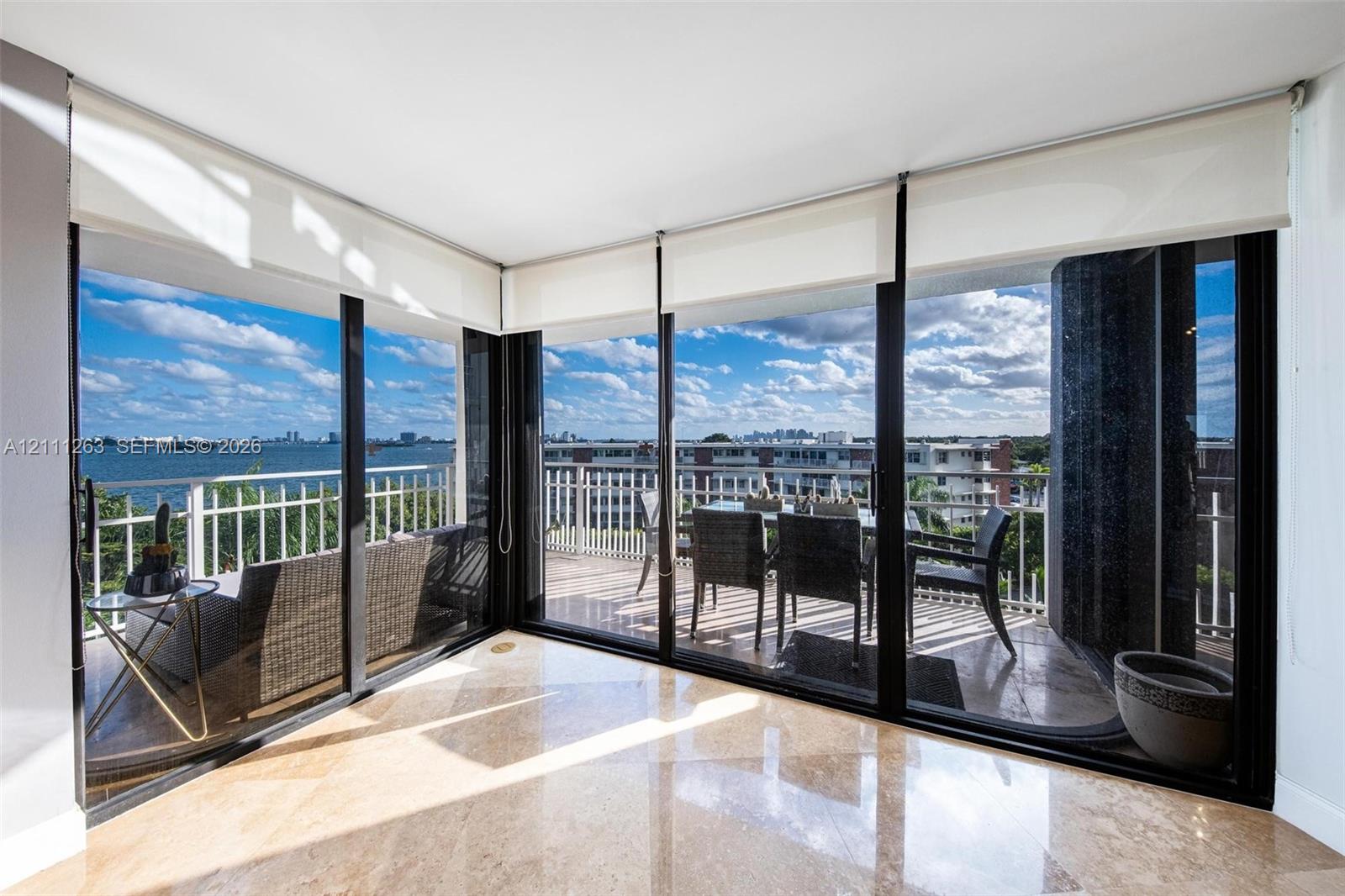 Floor-to-ceiling glass walls, polished stone flooring, and expansive wrap-around balcony with white metal railings