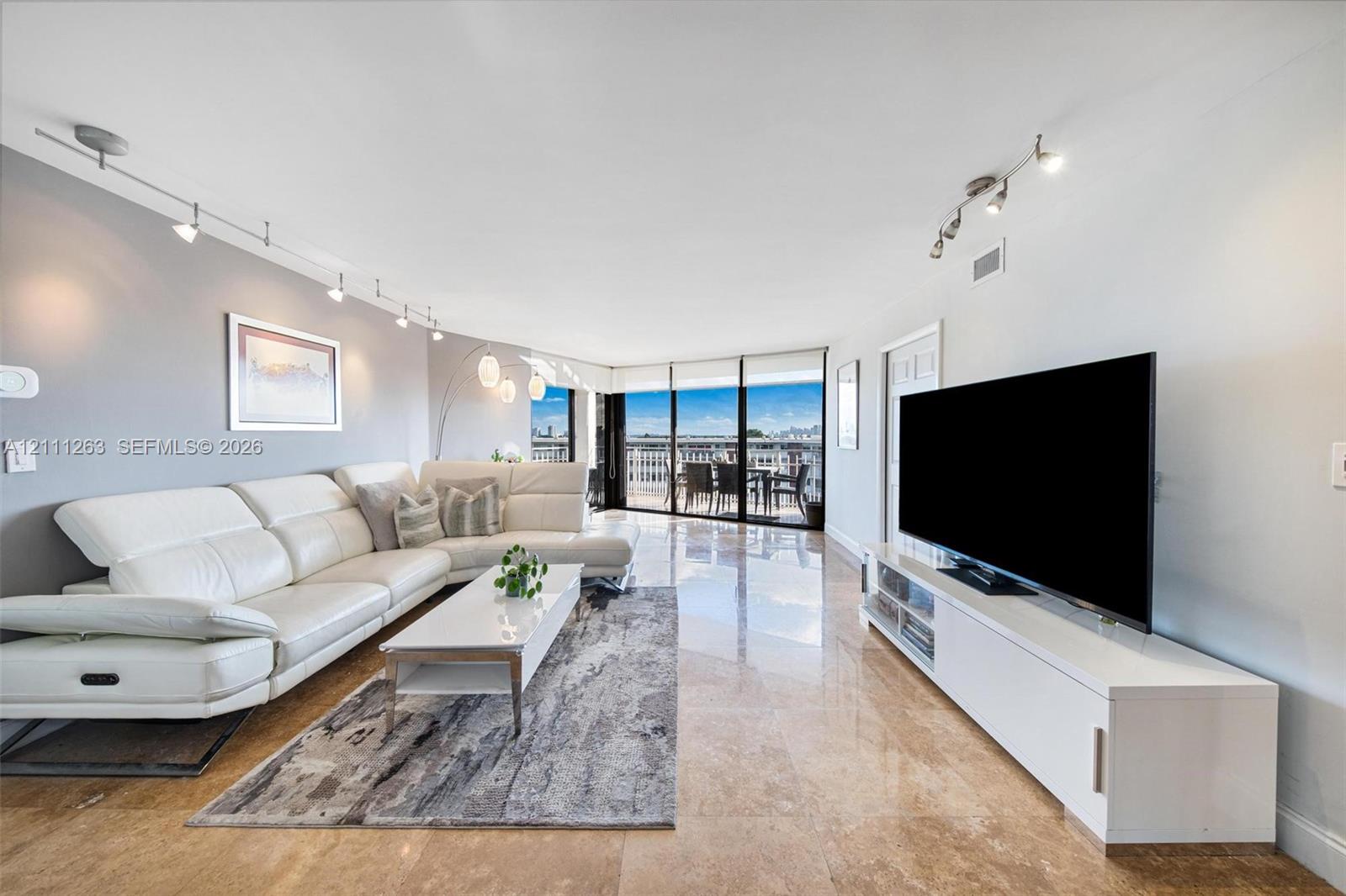 Living space featuring polished stone flooring, floor-to-ceiling glass sliding doors, track lighting, and a painted accent wall