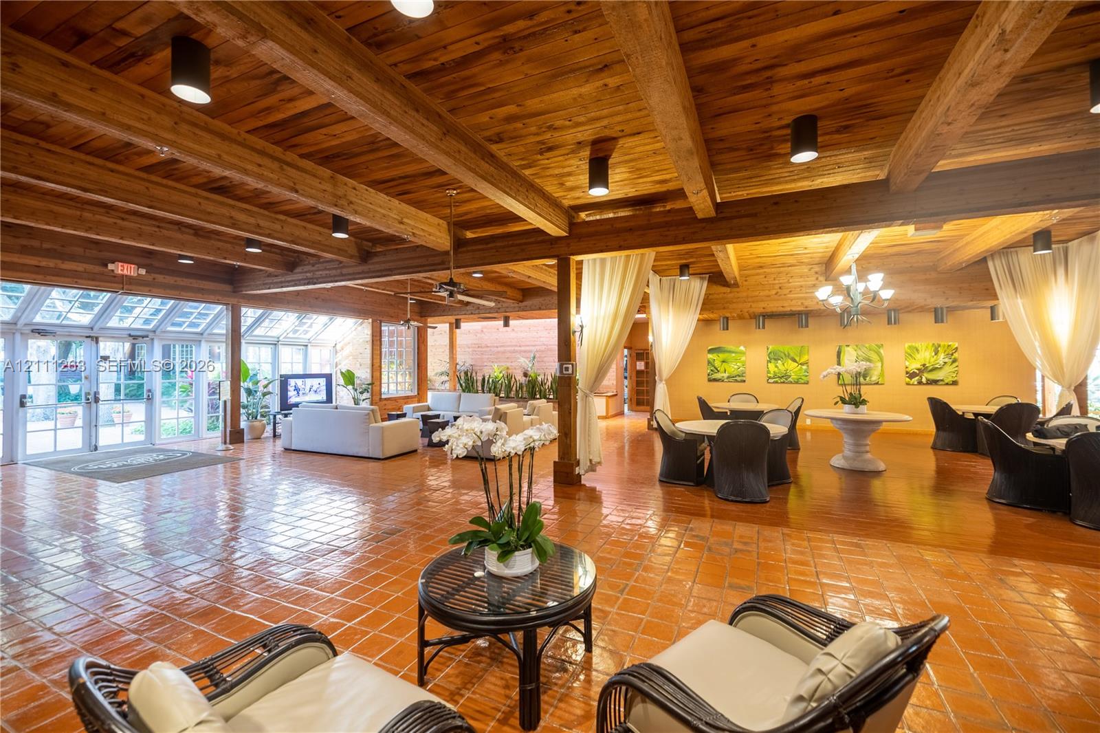 Expansive interior space featuring exposed wood-beam ceilings, clay tile flooring, and floor-to-ceiling glass panel walls