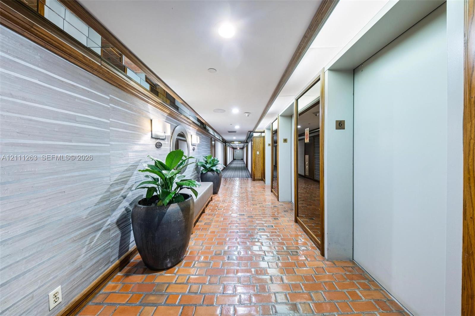 Hallway featuring brick flooring, textured wall covering, wood-trim detailing, mirrored panels, and recessed ceiling lighting