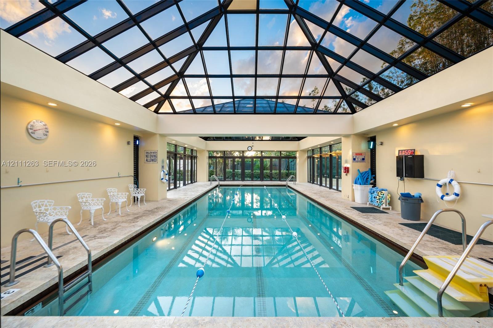Indoor swimming pool enclosure featuring a vaulted glass atrium roof, natural stone tile decking, and full-length glass paneled walls