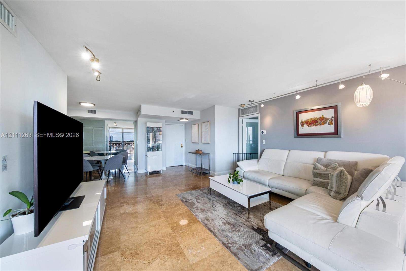 Open-concept living space featuring large-format tile flooring, track lighting, and a neutral color palette