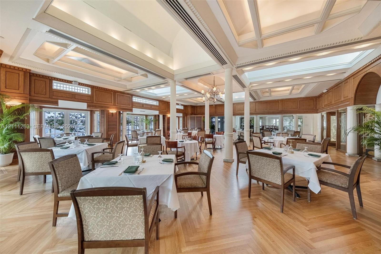 Expansive interior featuring high coffered ceilings with recessed lighting, herringbone wood-finish flooring, custom wood wall paneling, and structural columns