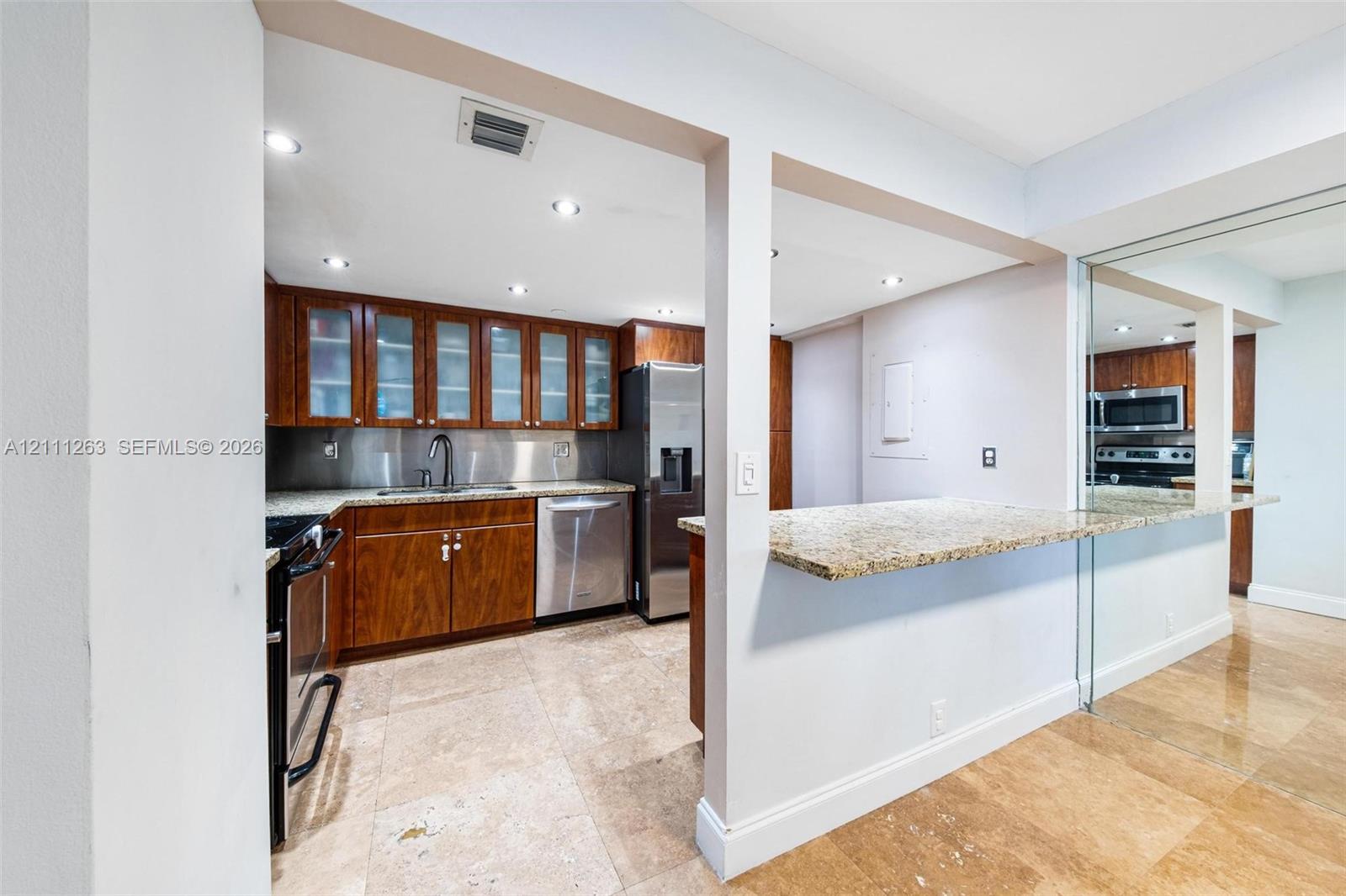 Kitchen featuring stone-finish countertops, stainless steel appliances, upper cabinetry with glass-panel doors, stone-tile flooring, and a stone-topped breakfast bar