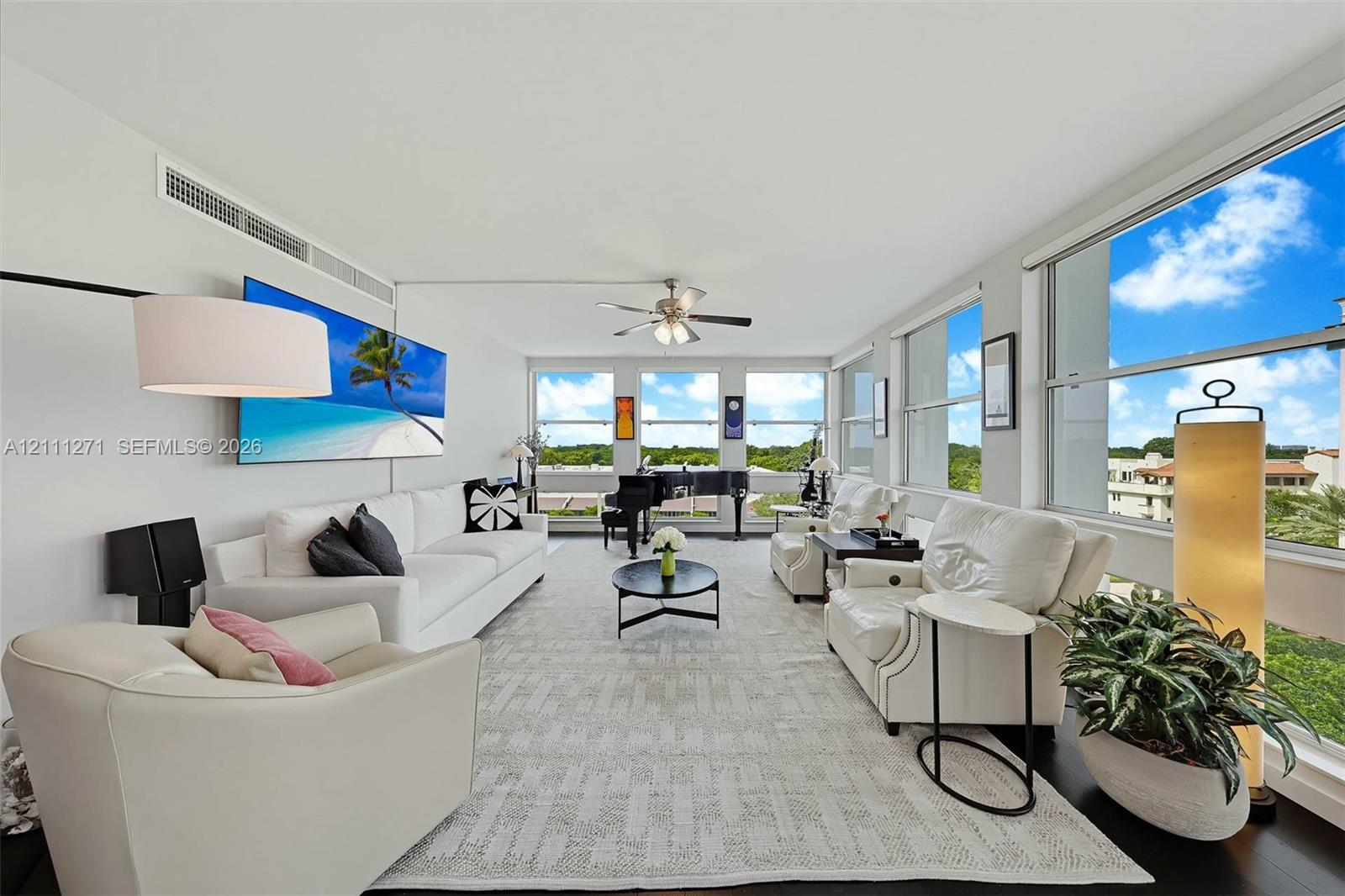 Living area featuring floor-to-ceiling windows, dark wood-finish flooring, and a ceiling fan with integrated lighting Living area featuring floor-to-ceiling windows, dark wood-finish flooring, and a ceiling fan with integrated lighting