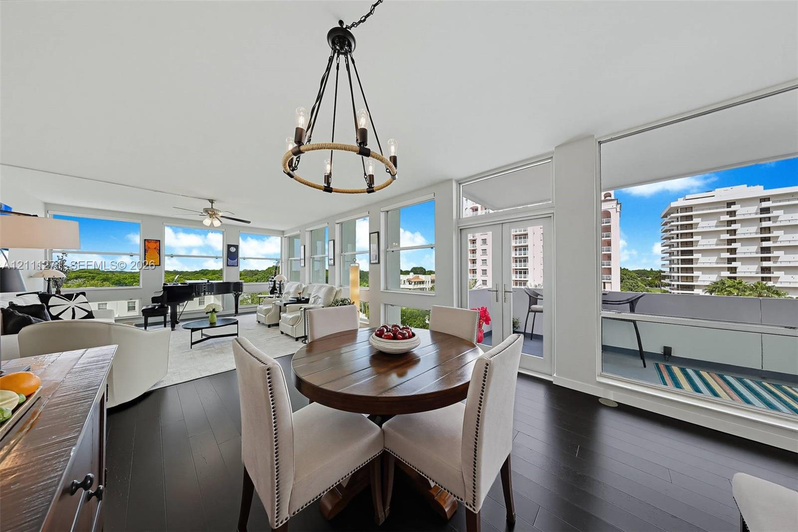 Living area featuring dark wood-finish flooring, a circular rope-accented chandelier, expansive floor-to-ceiling windows, and double glass doors opening to a balcony Living area featuring dark wood-finish flooring, a circular rope-accented chandelier, expansive floor-to-ceiling windows, and double glass doors opening to a balcony