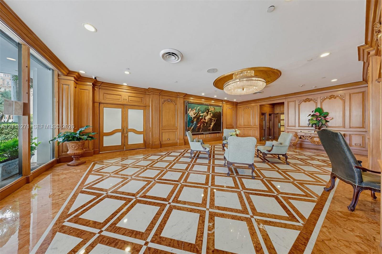 Geometric stone inlay flooring, extensive custom wood wall paneling, ornate ceiling medallion with integrated chandelier, and full-height glass-paneled entry doors