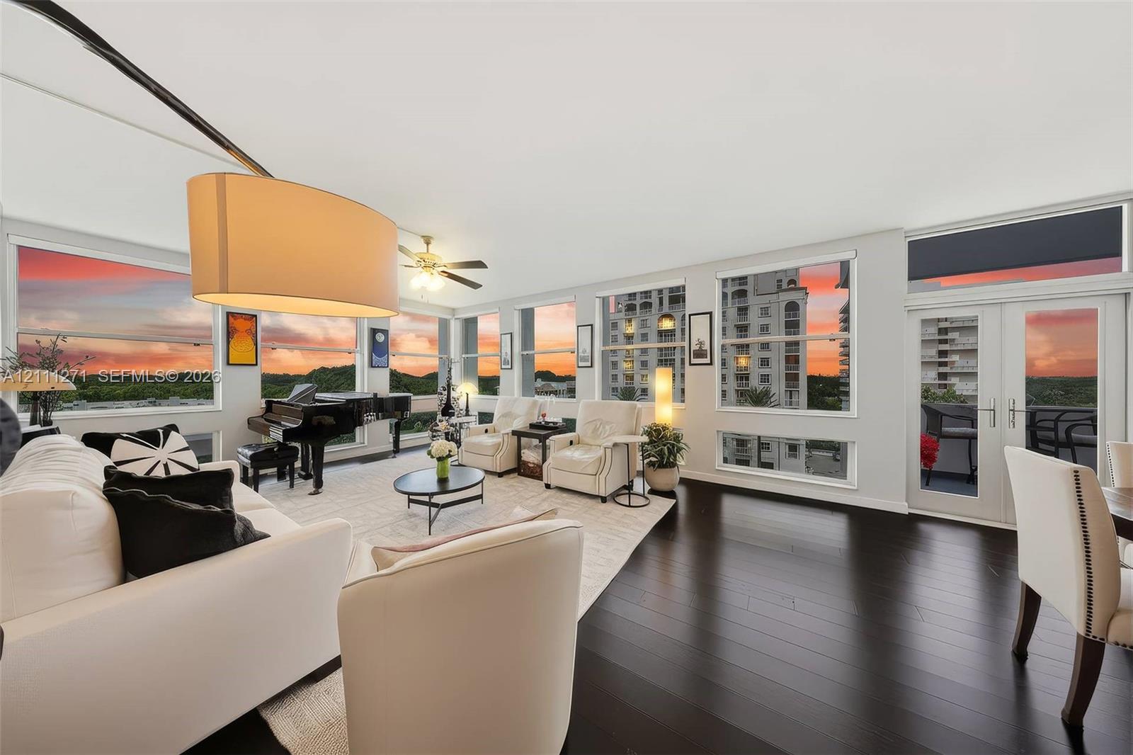 Living area featuring expansive window walls, dark wood-finish flooring, ceiling fan, and access to a private balcony Living area featuring expansive window walls, dark wood-finish flooring, ceiling fan, and access to a private balcony