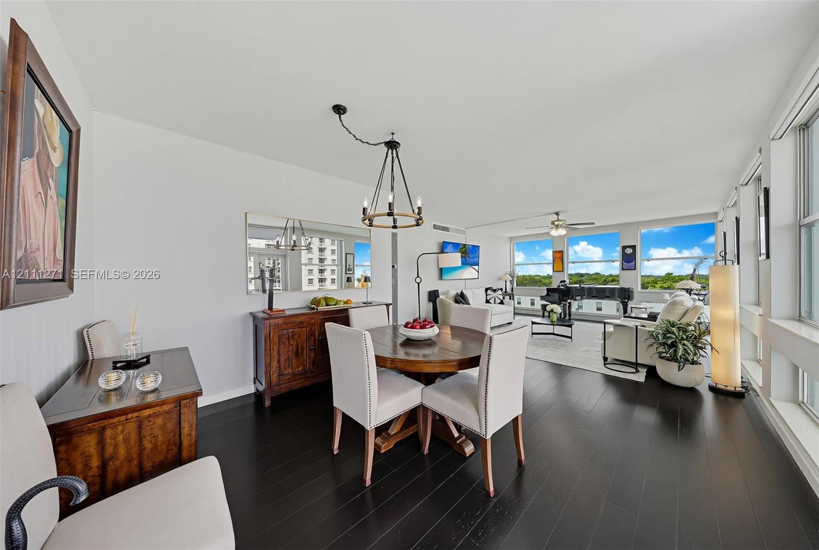 Open-concept living space featuring wood-finish flooring, a wall-mounted mirror, a multi-arm chandelier, and expansive windows Open-concept living space featuring wood-finish flooring, a wall-mounted mirror, a multi-arm chandelier, and expansive windows