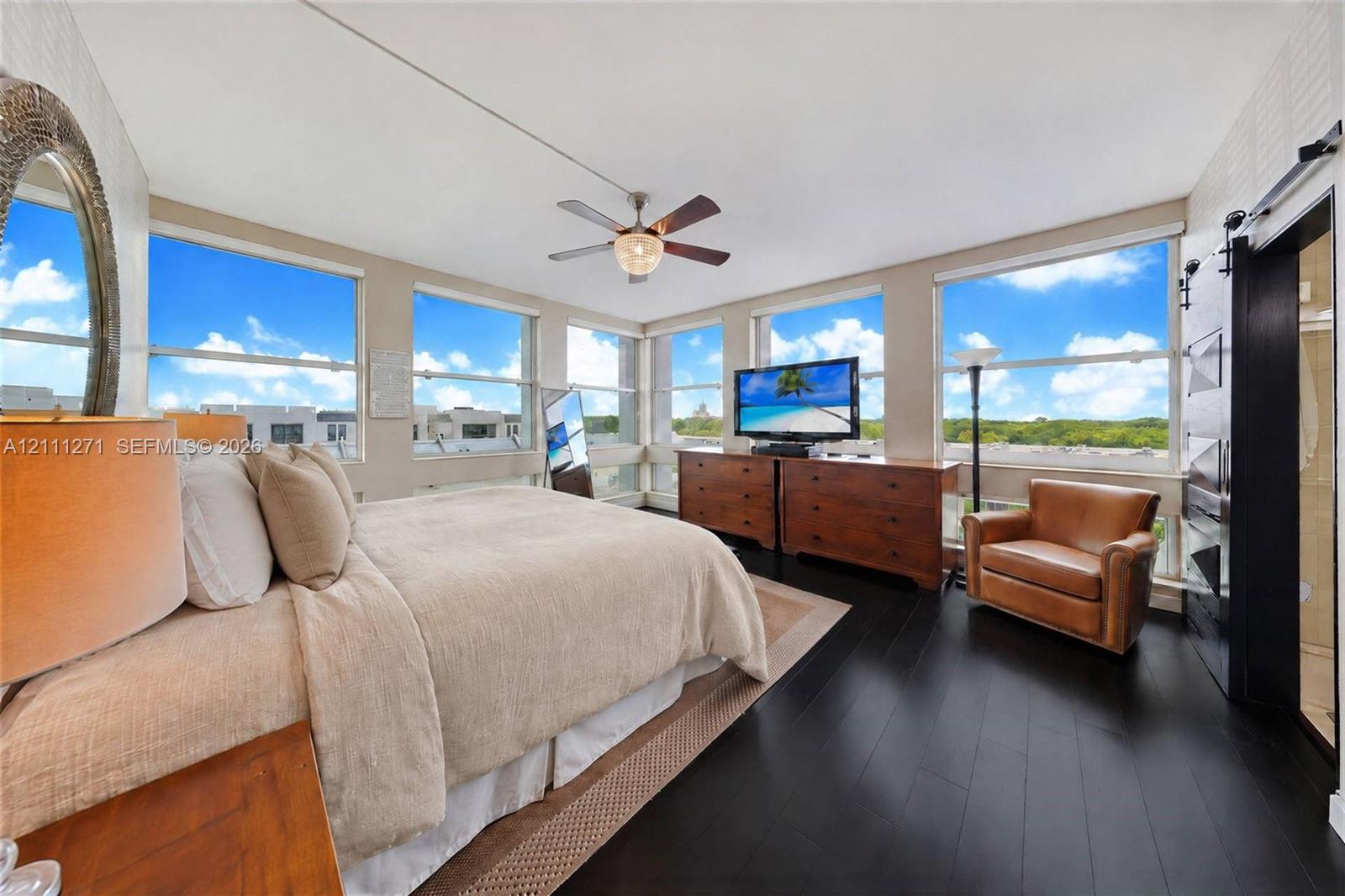 Expansive floor-to-ceiling windows, dark wood-finish flooring, ceiling fan with integrated lighting, and black sliding barn door