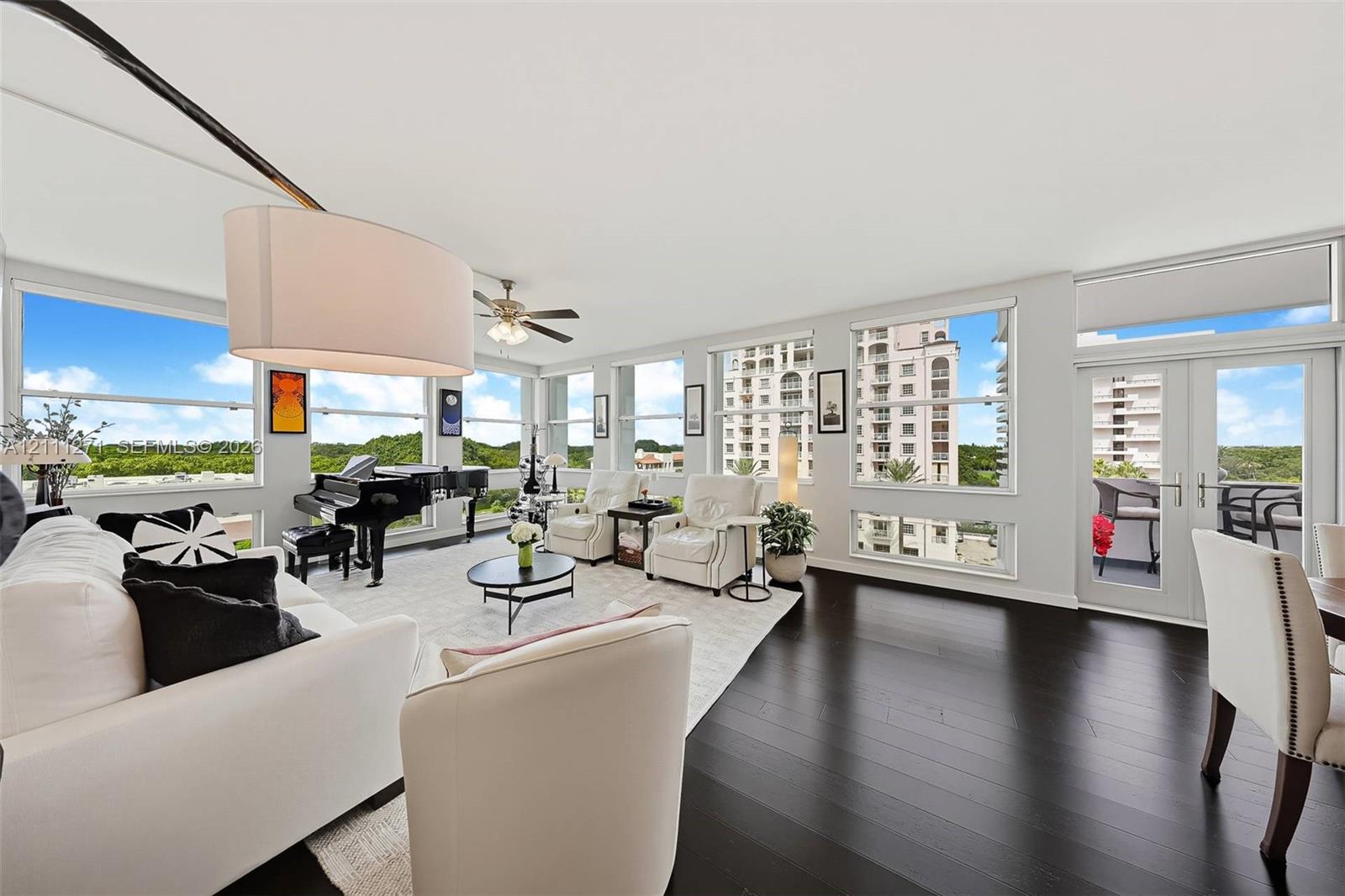 Open-concept living area featuring dark wood-finish flooring, floor-to-ceiling windows, a ceiling fan, and double-glass doors leading to a balcony Open-concept living area featuring dark wood-finish flooring, floor-to-ceiling windows, a ceiling fan, and double-glass doors leading to a balcony