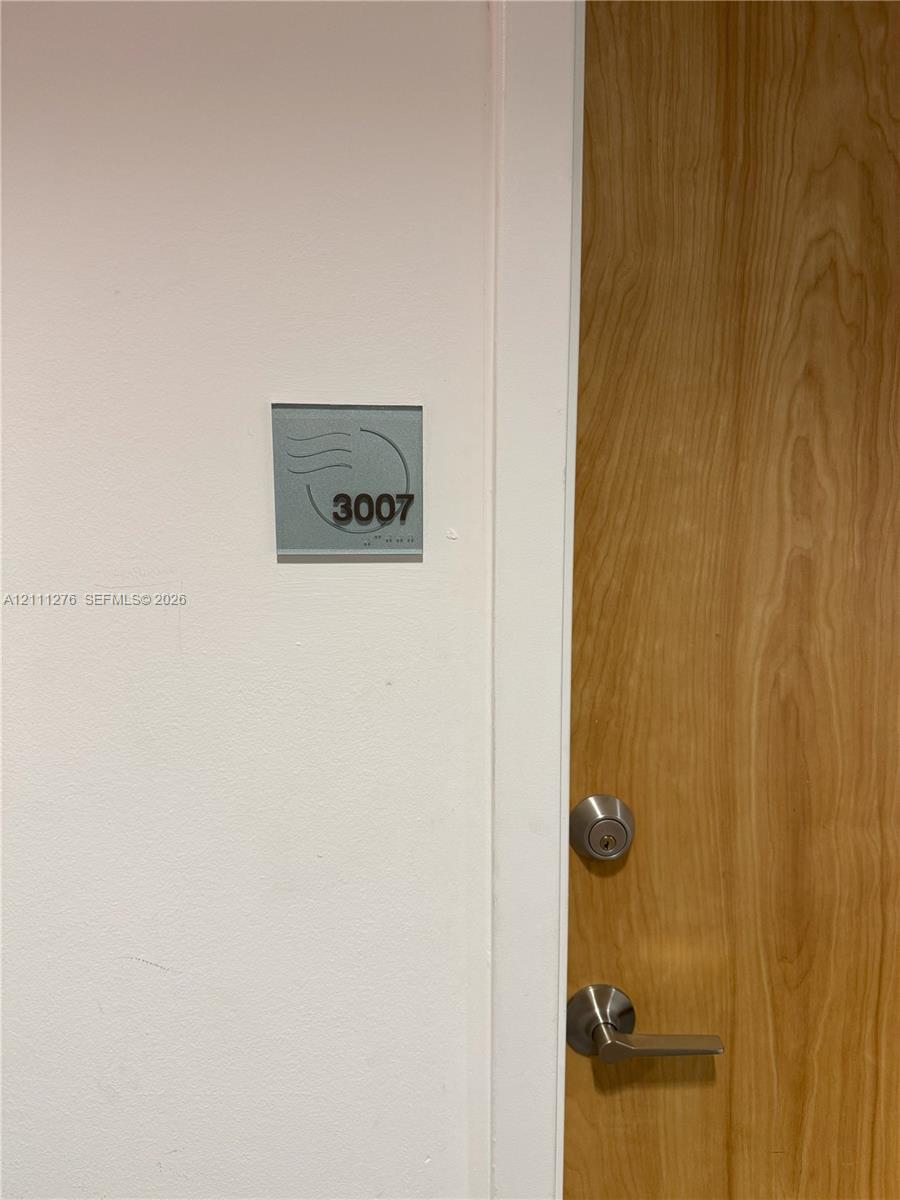 Solid wood-finish door with brushed nickel lever handle and deadbolt, featuring an acrylic wall-mounted suite sign