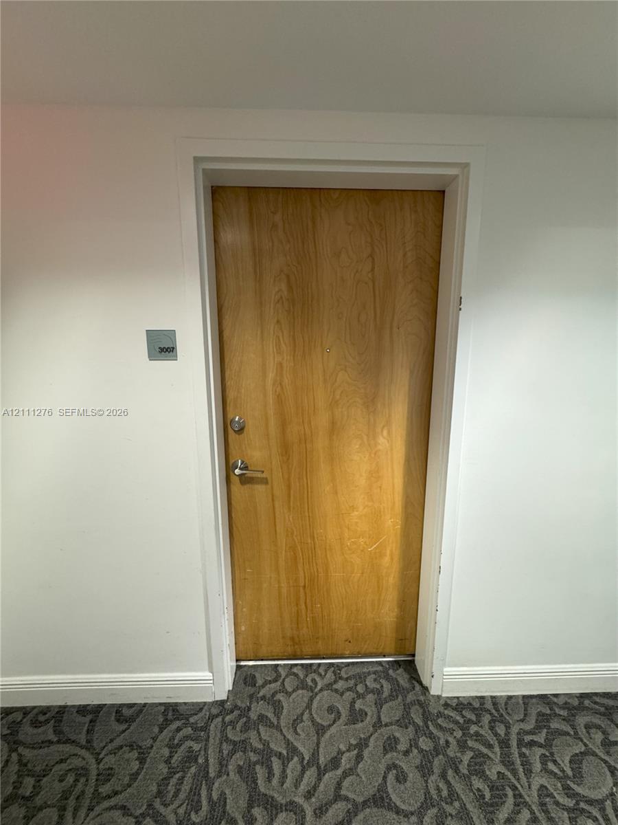 Solid wood-finish door with brushed nickel lever handle and deadbolt, featuring an acrylic wall-mounted suite sign