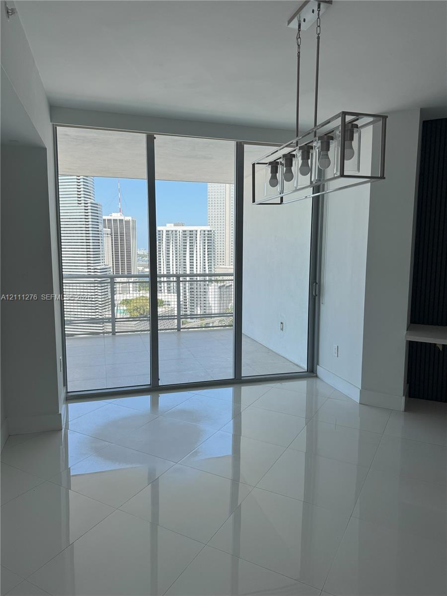 Floor-to-ceiling glass panels, expansive covered balcony, polished tile flooring, and geometric metal-frame chandelier