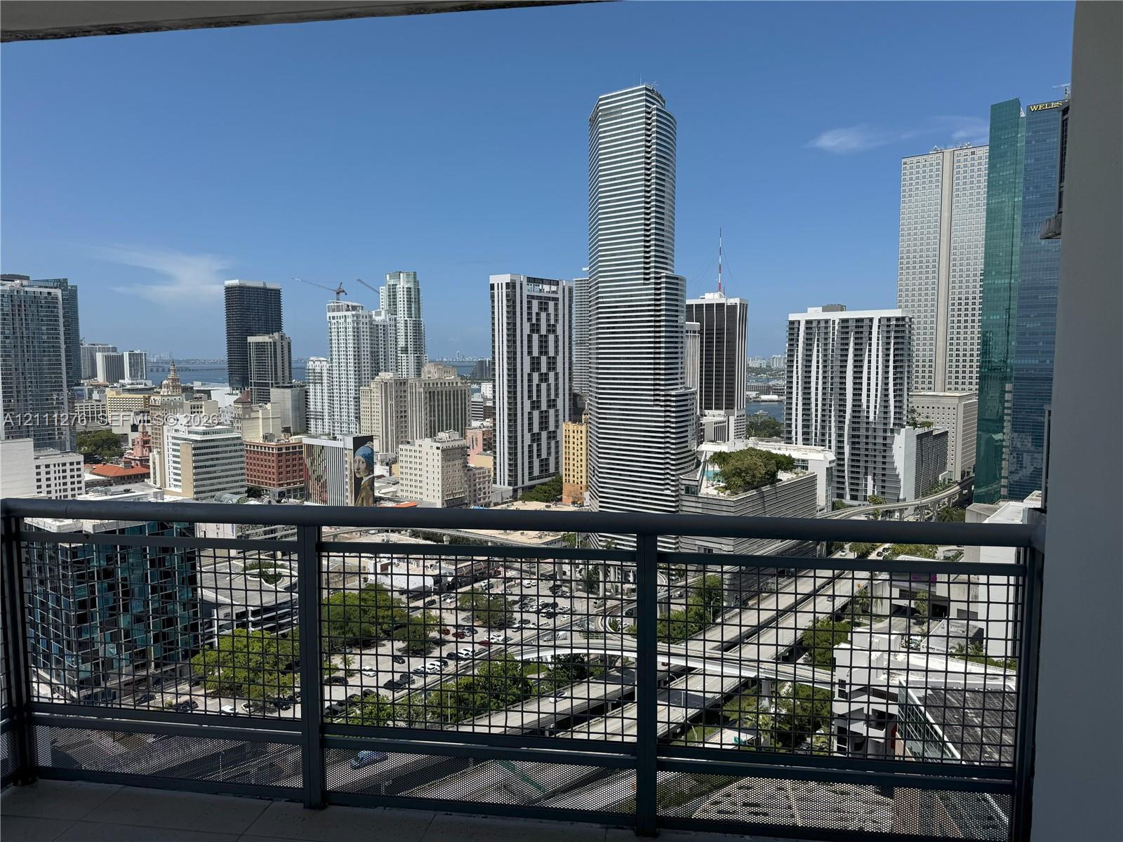 Private balcony featuring a dark metal mesh railing and tile flooring overlooking a cityscape Private balcony featuring a dark metal mesh railing and tile flooring overlooking a cityscape