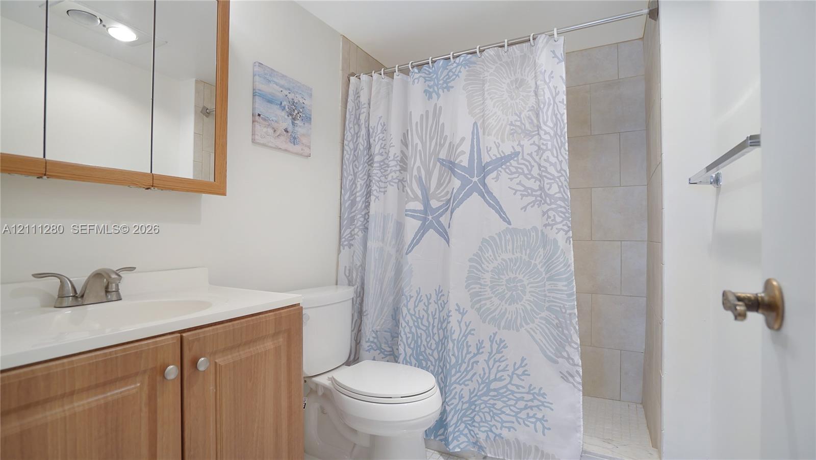 Wood-finish vanity cabinet with a solid-surface integrated sink, mirrored medicine cabinet, and tiled shower surround