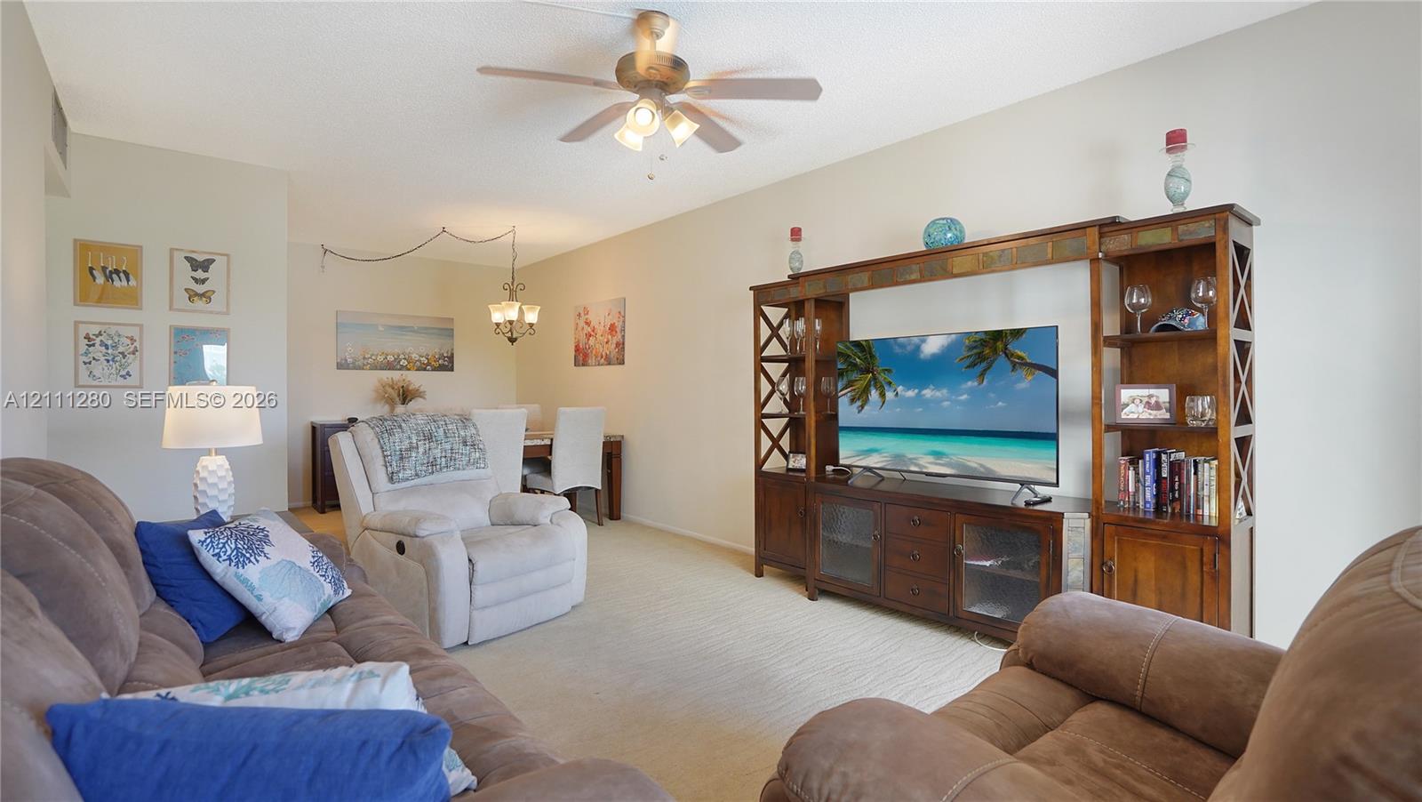 Living area featuring neutral carpeting, a ceiling fan with integrated lighting, and a multi-tiered decorative light fixture