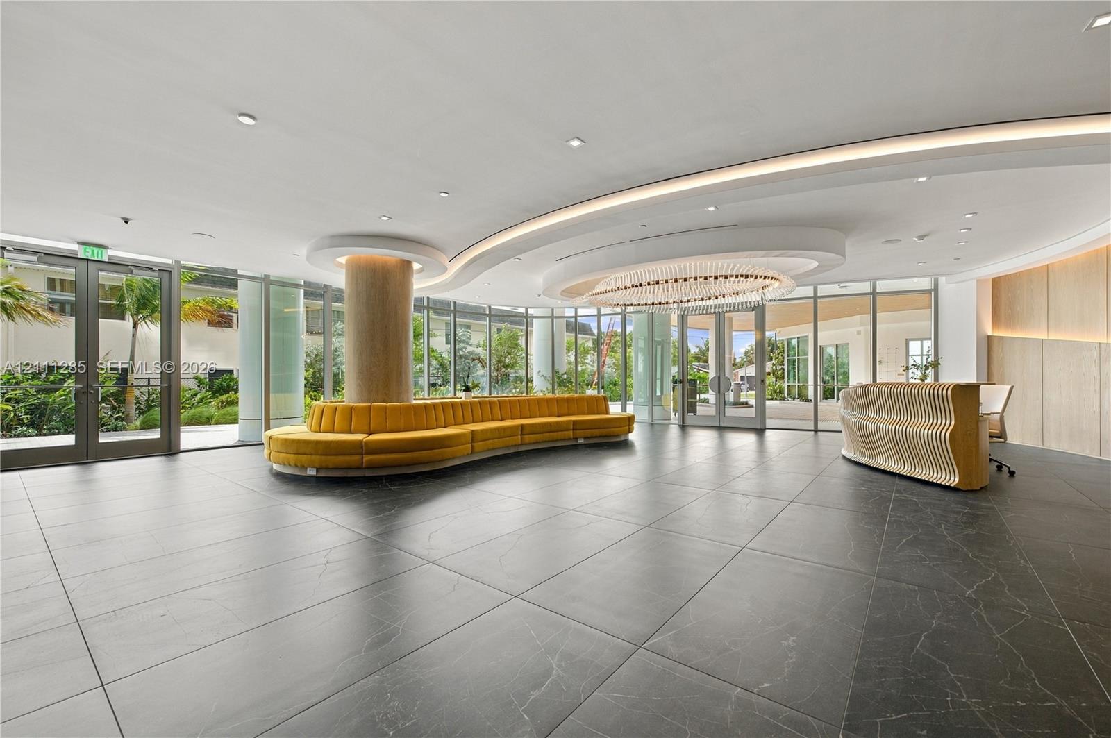 Lobby featuring large-format dark stone flooring, floor-to-ceiling glass walls, recessed cove lighting, and a circular chandelier