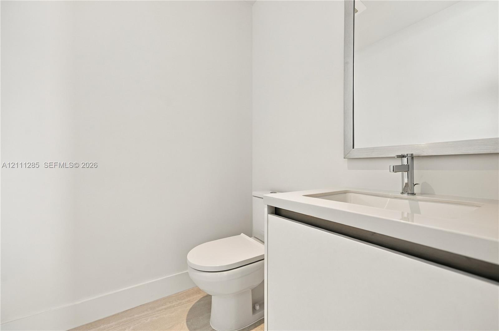 Modern vanity featuring a seamless integrated countertop and sink, wall-mounted mirror with a metallic frame, chrome faucet, and light-toned wood-finish flooring