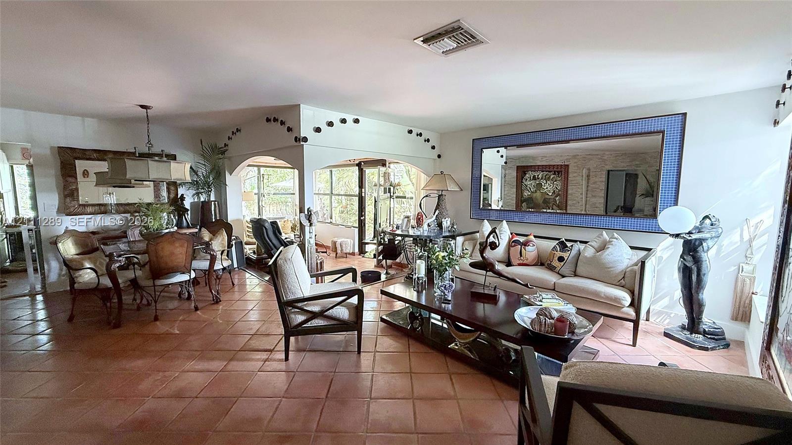 Open living area featuring large-format terra-cotta tile flooring, architectural arched openings, and a large decorative wall mirror with a blue mosaic frame Open living area featuring large-format terra-cotta tile flooring, architectural arched openings, and a large decorative wall mirror with a blue mosaic frame