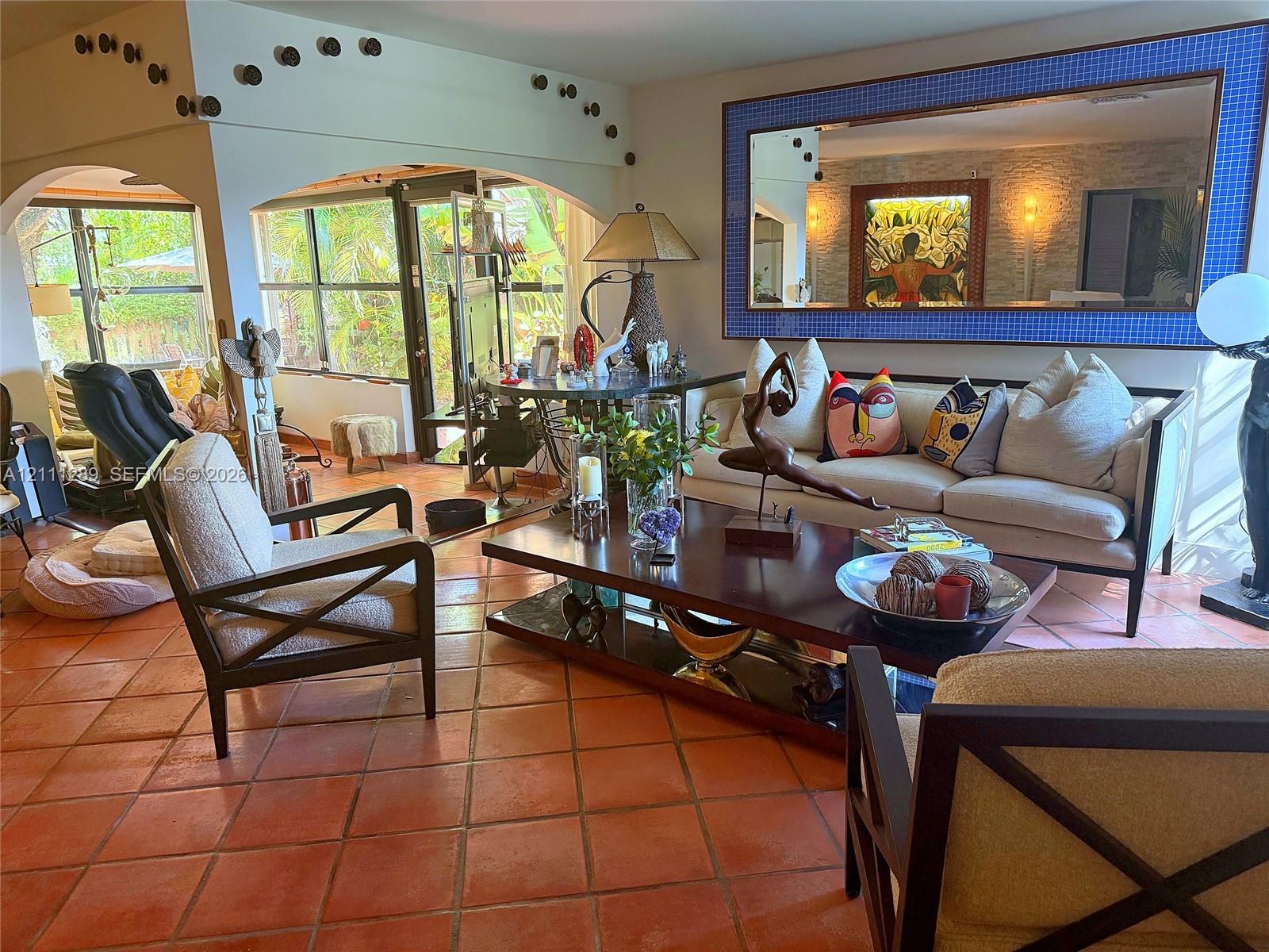 Living area featuring terracotta tile flooring, dual arched wall openings, and a large decorative wall mirror Living area featuring terracotta tile flooring, dual arched wall openings, and a large decorative wall mirror