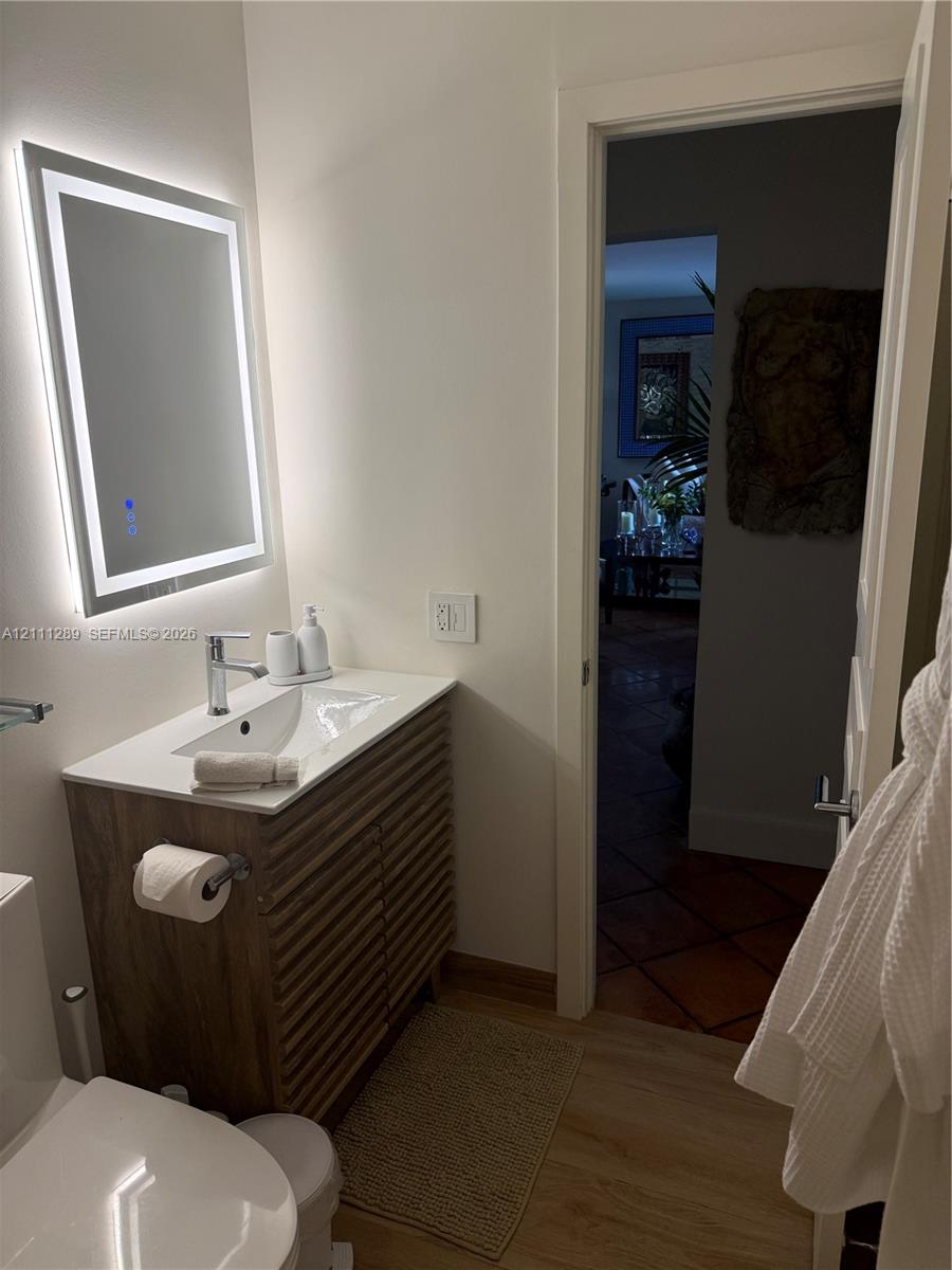 Wood-finish slatted vanity with a white countertop and integrated sink, paired with a modern LED-backlit mirror and a polished chrome single-handle faucet