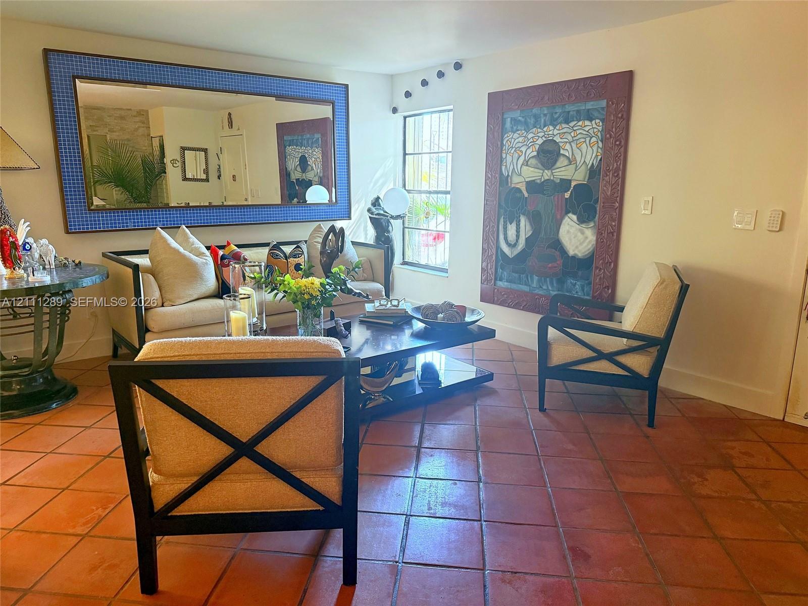 Terracotta tile flooring, large-format rectangular wall mirror with a textured blue frame, and multi-pane window with security bars Terracotta tile flooring, large-format rectangular wall mirror with a textured blue frame, and multi-pane window with security bars