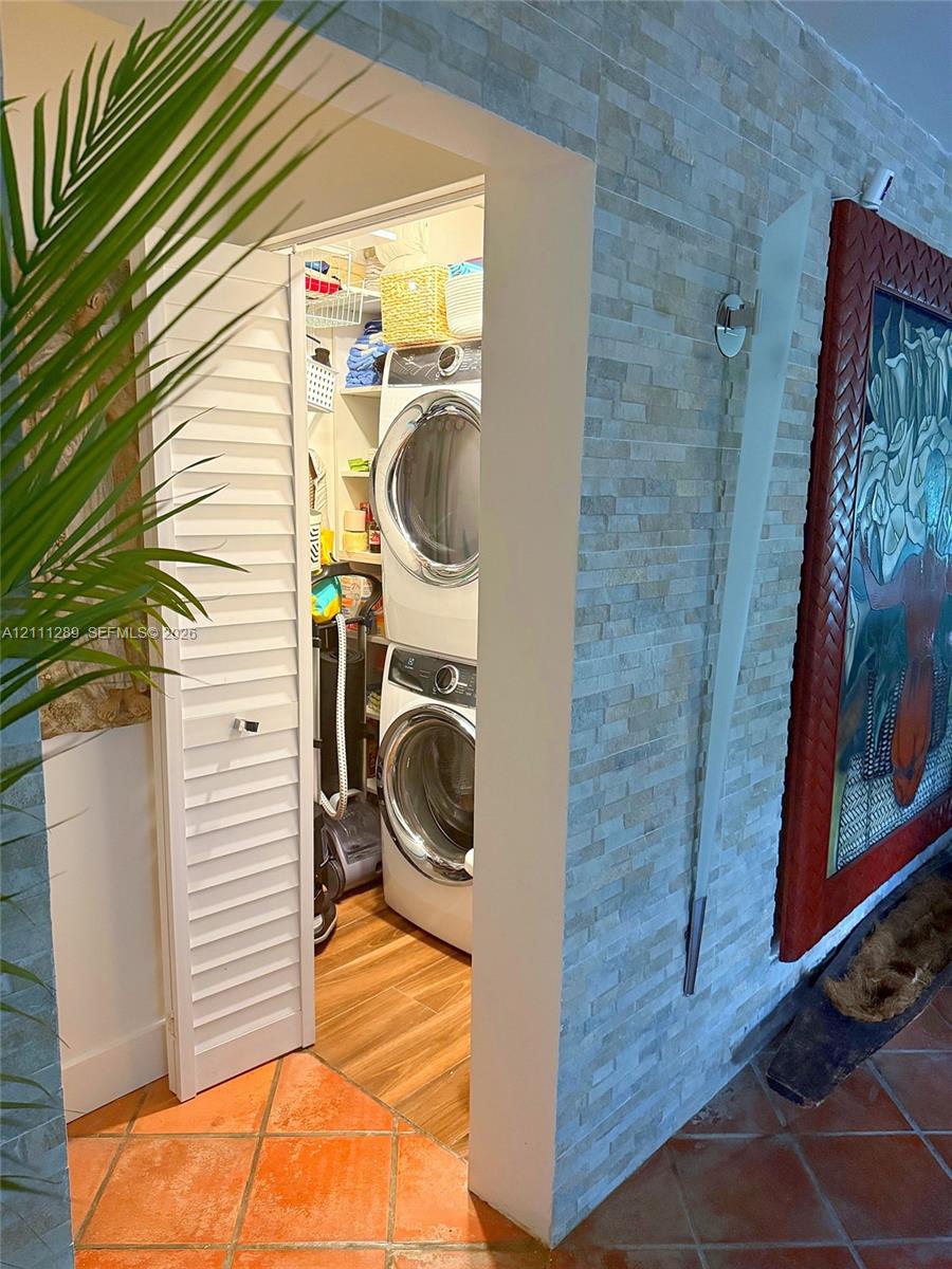 Laundry closet featuring white louvered doors, built-in shelving, and wood-finish flooring, contrasted by an exterior wall finished in stacked stone veneer