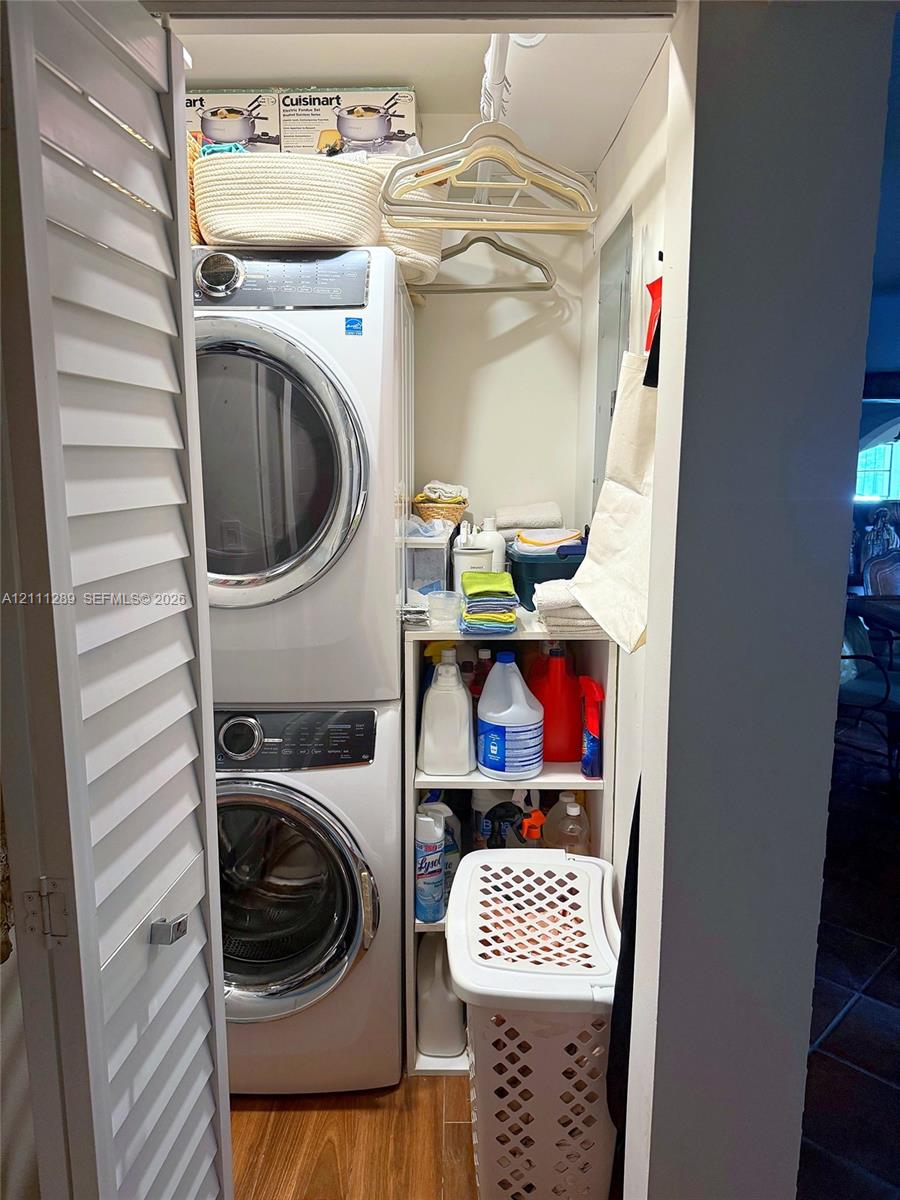 Laundry closet featuring stacked front-load washer and dryer, louvered bi-fold doors, wood-finish flooring, and built-in vertical shelving