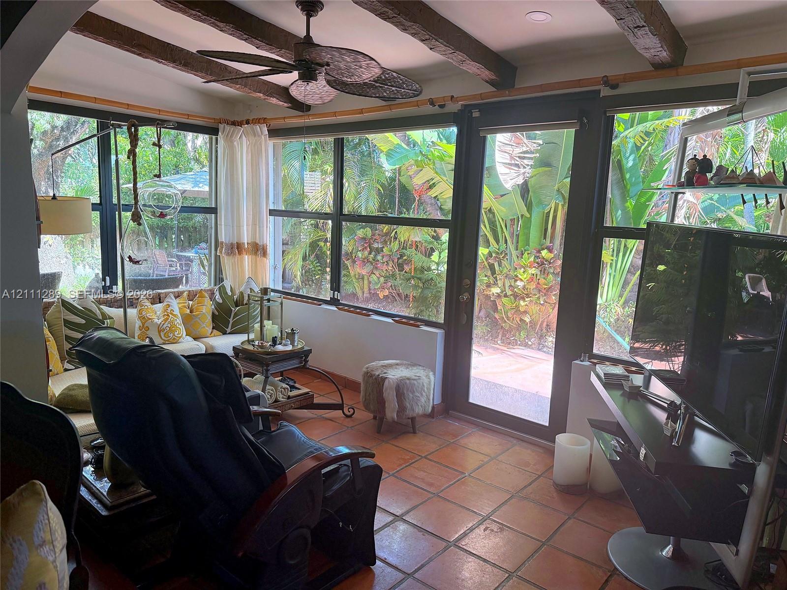 Sunroom featuring terra cotta tile flooring, exposed wood ceiling beams, floor-to-ceiling windows, and a ceiling fan with integrated lighting Sunroom featuring terra cotta tile flooring, exposed wood ceiling beams, floor-to-ceiling windows, and a ceiling fan with integrated lighting