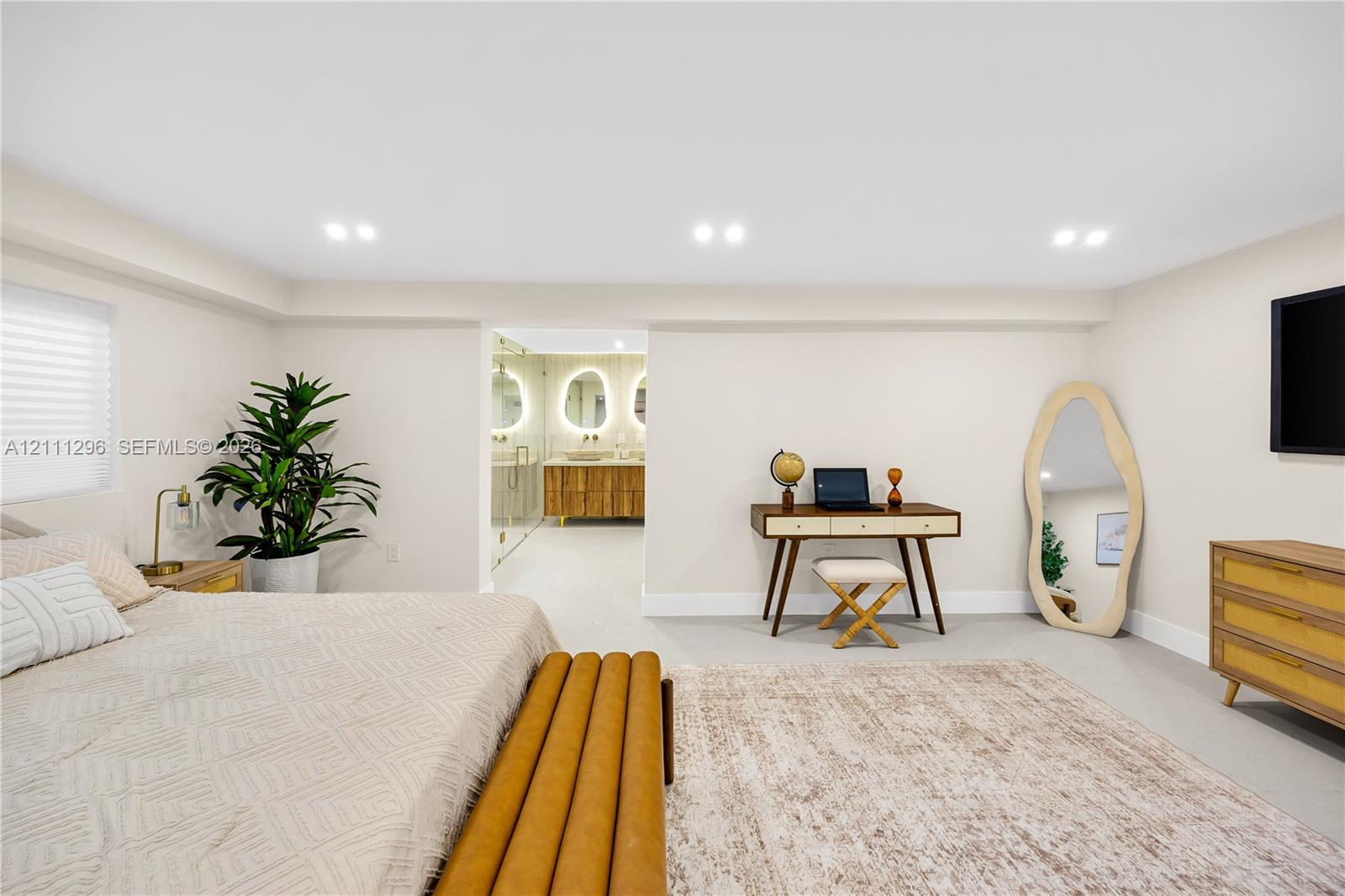Neutral-toned room featuring recessed ceiling lighting, light-colored tile flooring, and integrated access to a bathroom with a double-sink vanity and illuminated mirrors