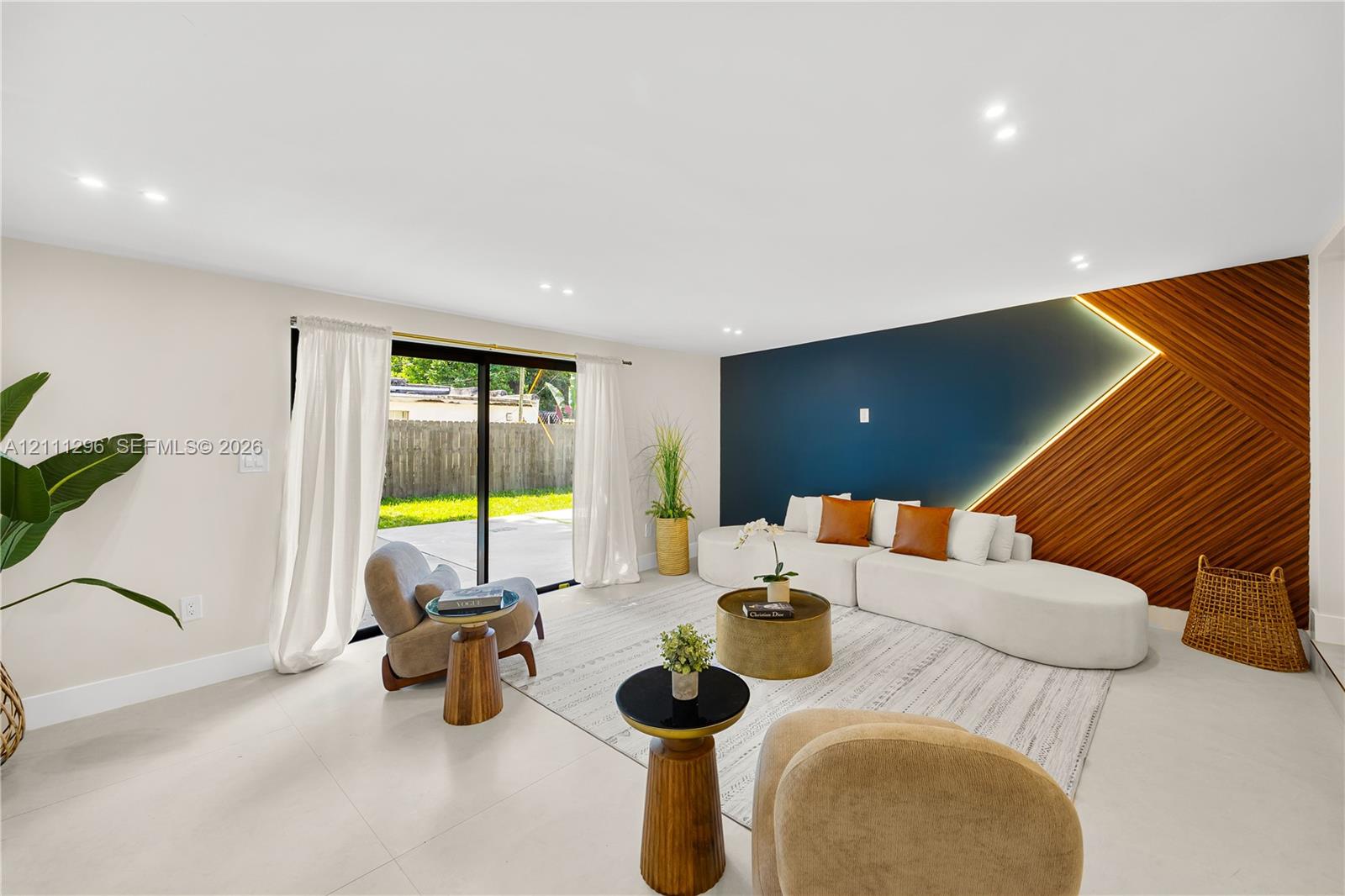 Large-format neutral tile flooring, accent wall with geometric wood paneling, integrated recessed lighting, and expansive sliding glass doors